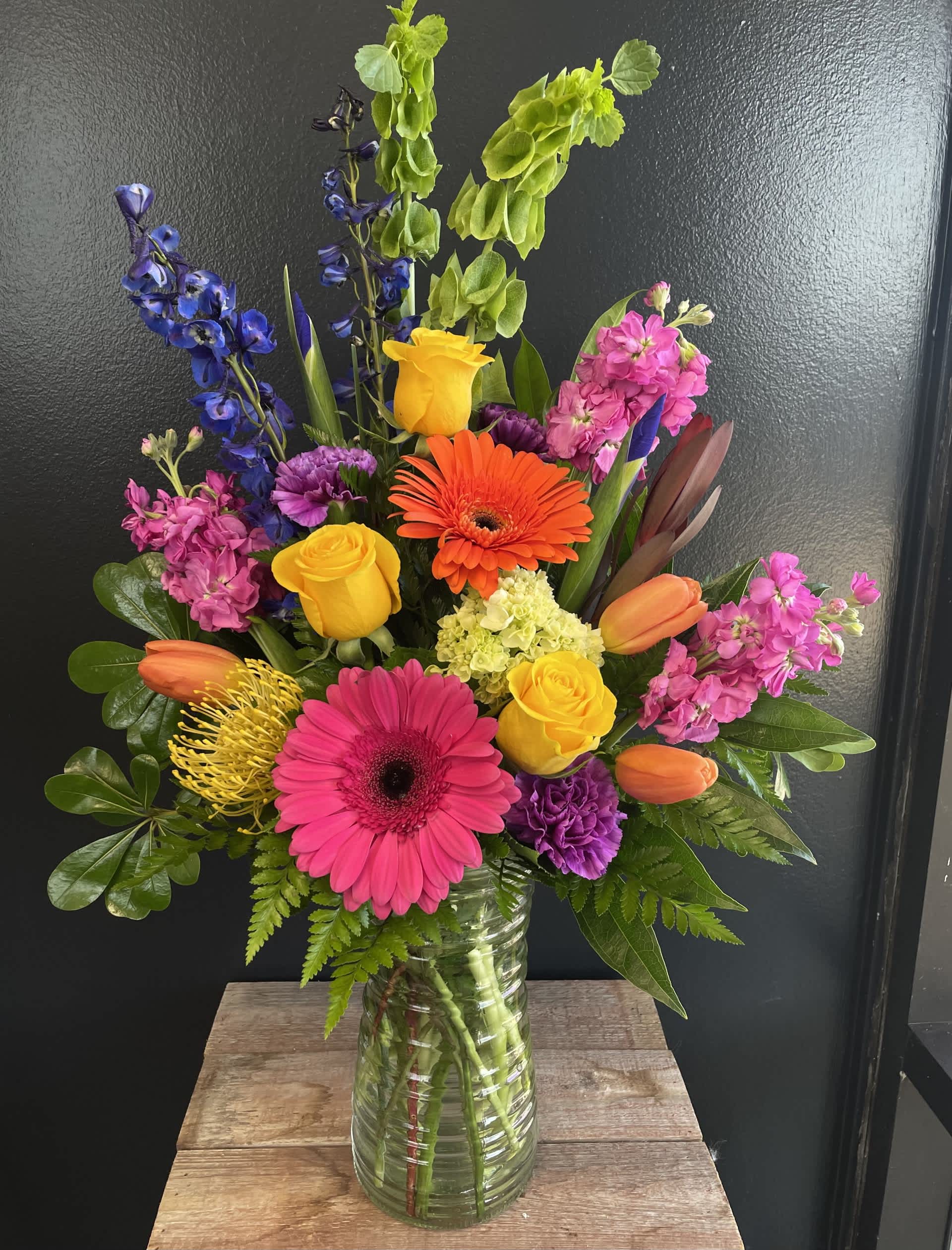 Bold &amp; Beautiful  - A bold, moody fresh arrangement built around gerbera daisies blends high‑impact color with deep, dramatic undertones. Instead of the bright, cheerful vibe gerberas usually give, the palette and supporting flowers shift the design into something richer, more atmospheric, and emotionally intense. Colors may vary. 