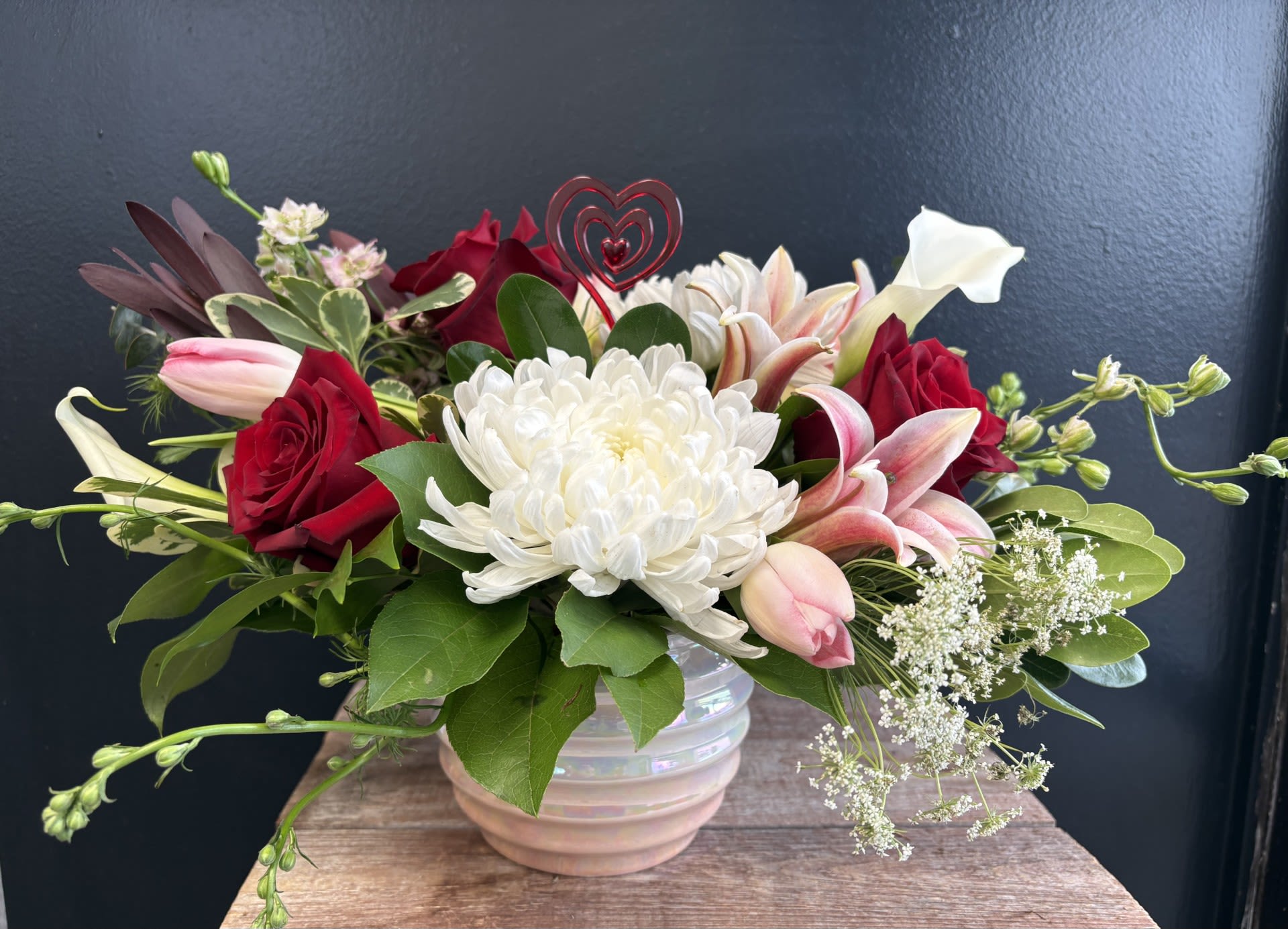 Love in Bloom  - Romance is still alive- this fresh arrangement that feels both romantic and joyfully vibrant. Rich red roses bring depth and passion, while snowy white blooms add a clean, luminous contrast.  Creating a harmonious blend of color that feels warm and affectionate. Containers may vary.