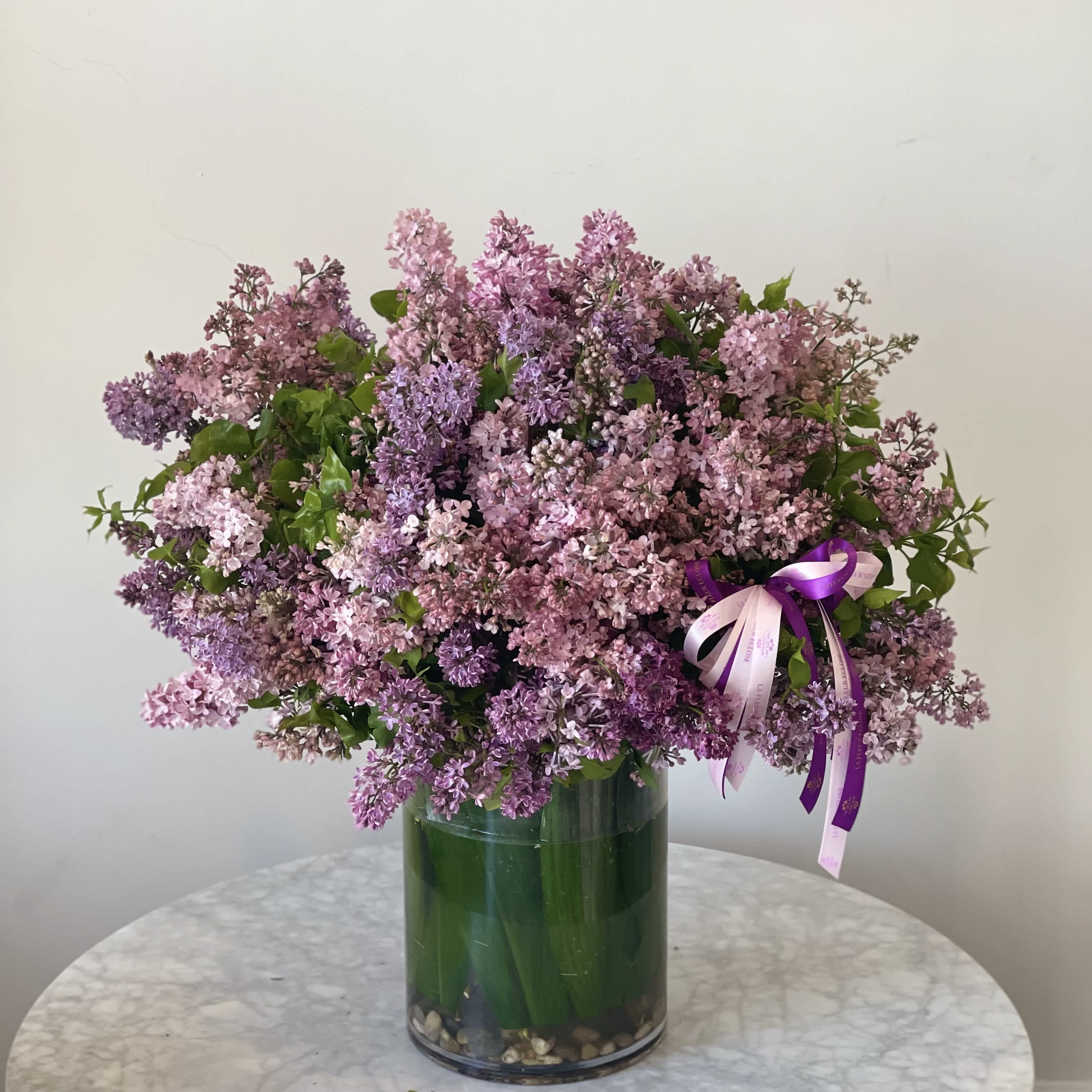Lilac Vase V - Known for its intoxicating fragrance and beautiful appearance, the lilac is a common flower with a powerful hidden meaning. Violet-colored lilies usually symbolize spirituality and fresh beginnings. This seasonal and unique arrangement is made of beautiful and scented lilac stems within our vase 