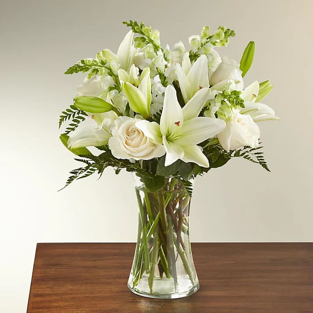 Eternal Friendship - White Roses, Asiatic lilies, and white snapdragons accented by lush greens arranged in a clear glass 8" vase.   An excellent choice for a wake, funeral service, or sending your condolences to the home of a grieving family.  Approximately 17"H x 14"W.   