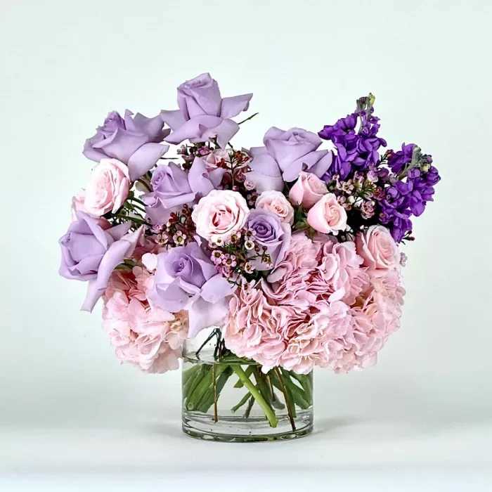La La La - Bring a touch of tranquility and beauty into your life or the lives of your loved ones with our Simply Pink and Lavender Blooms Bouquet. Elevate the ambiance of any space with this thoughtfully curated arrangement, designed to inspire moments of joy, love, and peaceful reflection.  This set includes:        Arrangement Size: 12" x 12"  pink hydrangeas, lavender roses, stock and wax-flower                                     Simply glass vase Flowers:  Lavender roses Hydrangeas Stock flower Wax flower