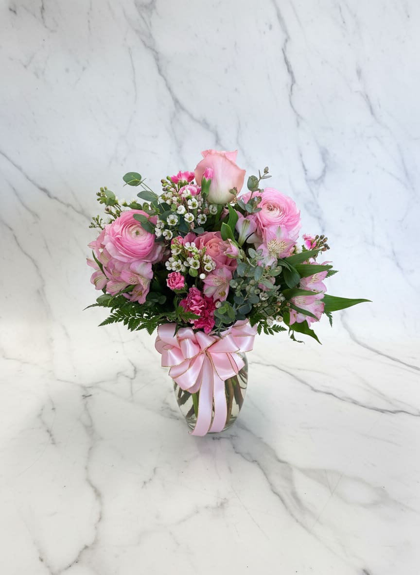 Cherry Tessino Vase - A vibrant pink vase arrangement featuring pink roses, pink ranunculus, white alstroemeria, cherry tessino carnations, wax flower, and fresh greenery. Bright, feminine, and full of texture, this arrangement is perfect for celebrating love or friendship.