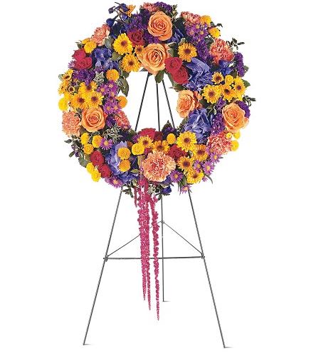 TF203-10  Celebration Wreath - This beautiful wreath with its distinctive orange, yellow and blue flowers, will offer your regards in the warmest way. One wreath arrives on a easel filled with orange roses, yellow spray chrysanthemums, blue hydrangea, red amaranthus and purple asters. Approximately 15" D 