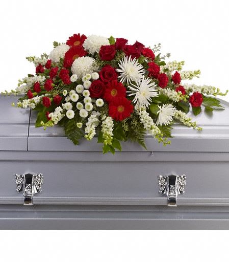Red and white casket spray with roses, chrysanthemums, and gerbera daisies on a silver casket