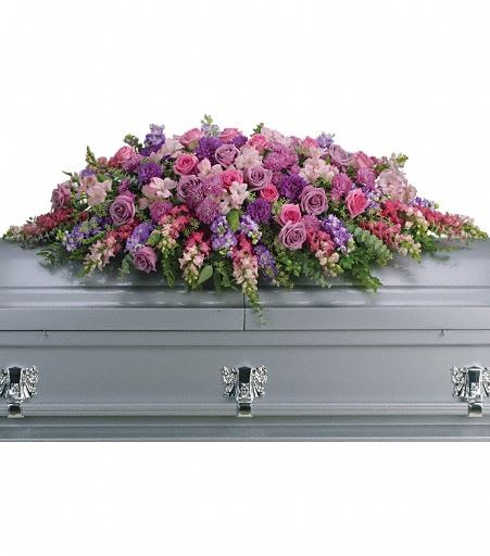 T235-2A Lavender Tribute Casket Spray - Like a heartfelt embrace, this beautiful casket spray delivers comfort and love in an extraordinary way. A wonderful array of lavender and pink flowers with just the right amount of greenery is a lovely way to pay tribute to someone who will always be with you in heart, mind and spirit. Lovely lavender and pink roses, snapdragons, alstroemeria, chrysanthemums, fern, eucalyptus and more create this tribute that is overflowing with grace and love. Approximately 51" W x 22" H 