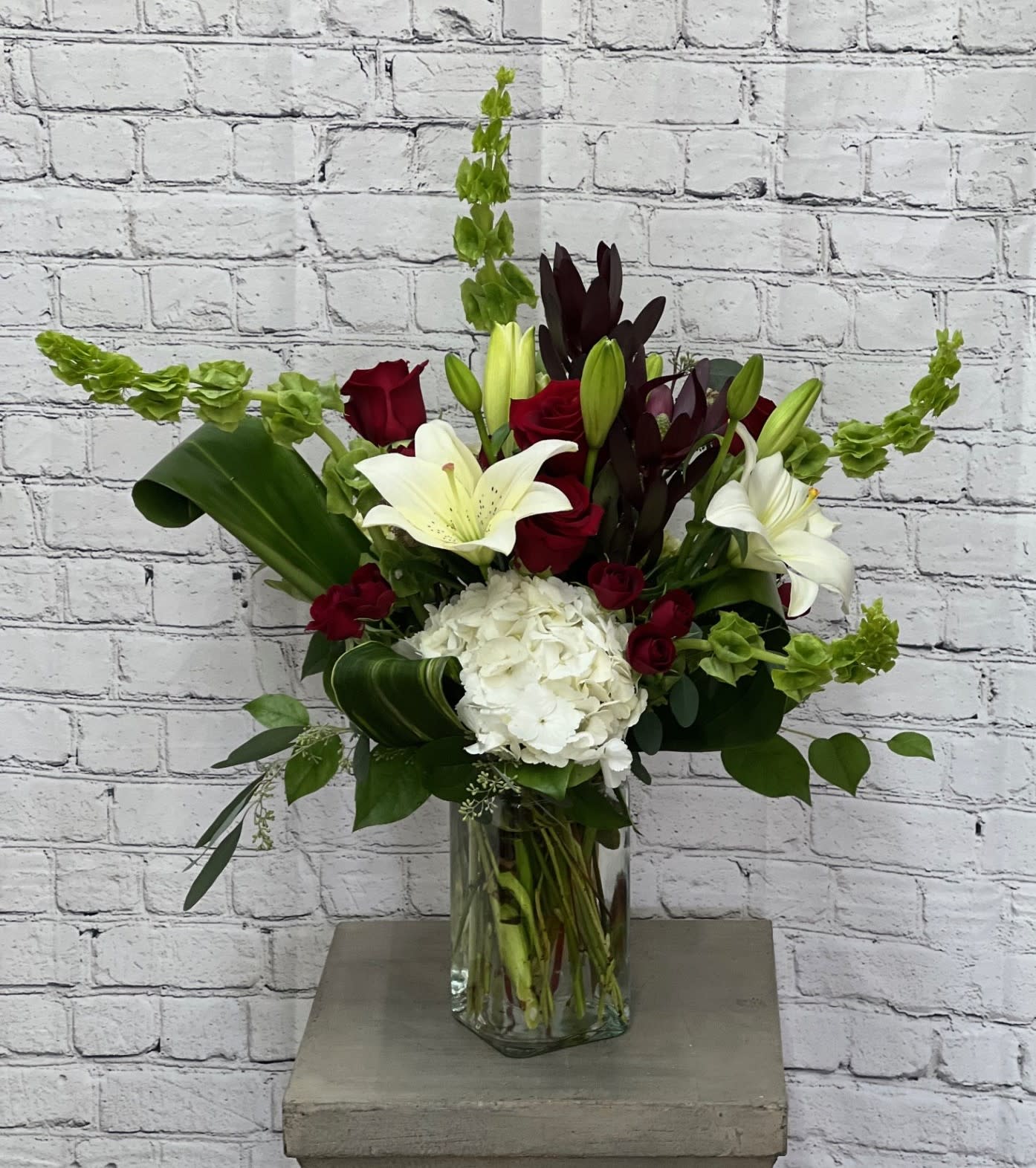 Love's Kiss - Send a kiss to your loved one with this beautiful vase arrangement filled with Red Roses, White Lilies and Hydrangeas, Safari Sunset, Bells of Ireland with lush greenery consisting of seeded eucalyptus, salal and aspidistra. 