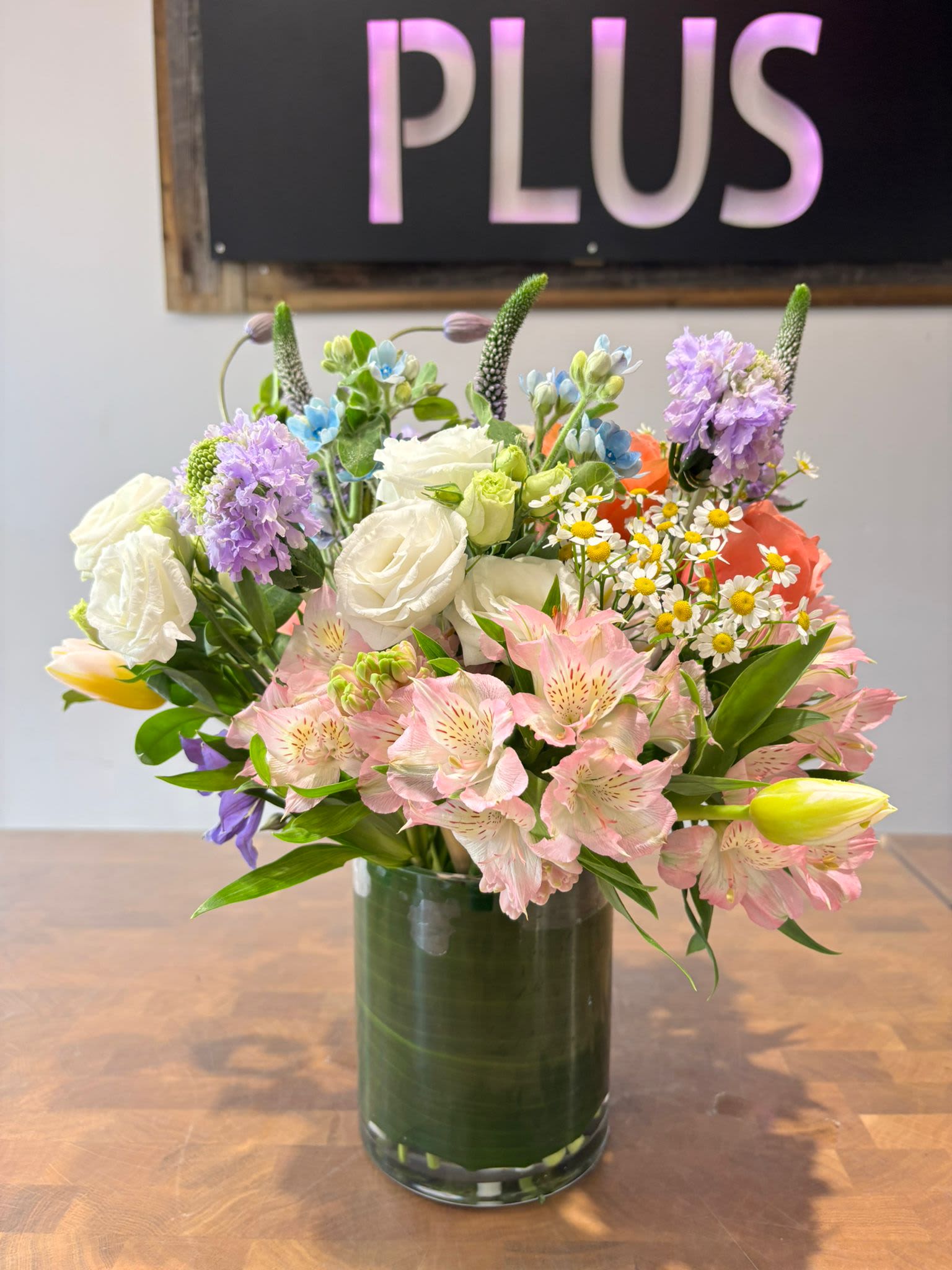 Garden Mix Arrangement (BP3) - A lush garden mix featuring pink alstroemeria, white lisianthus, and purple hyacinth. Accented with yellow tulips, tiny daisies, and set in a clear glass vase with a leaf lining.  Note on Seasonality: The arrangement shown features Tulips (available spring).