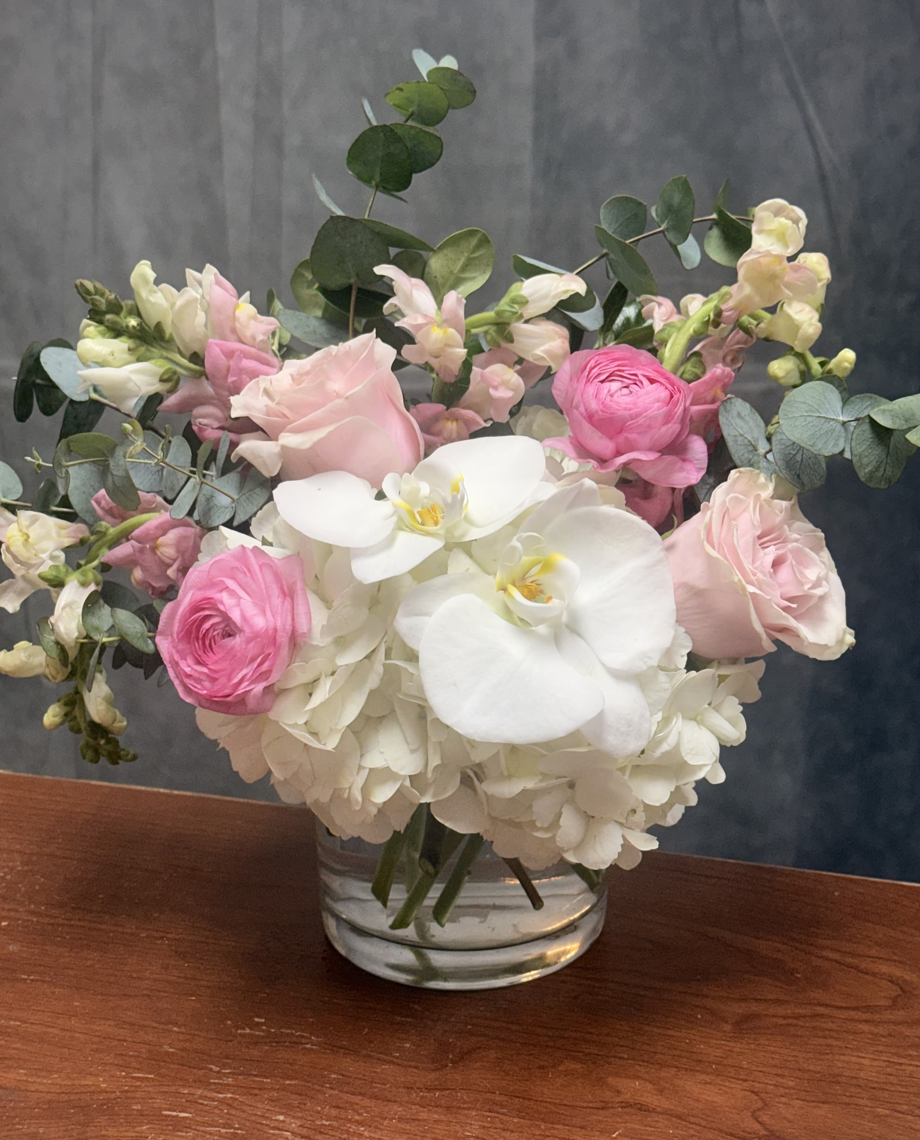 Soft  Elegance  - Introducing Soft Elegance —a breathtaking new design that blends timeless beauty with a touch of sophistication. Featuring lush hydrangeas, delicate orchids, fragrant stock, vibrant roses, graceful delphinium, and charming ranunculus, all arranged in a sleek low vase. Perfect for adding effortless elegance to any space or occasion. 