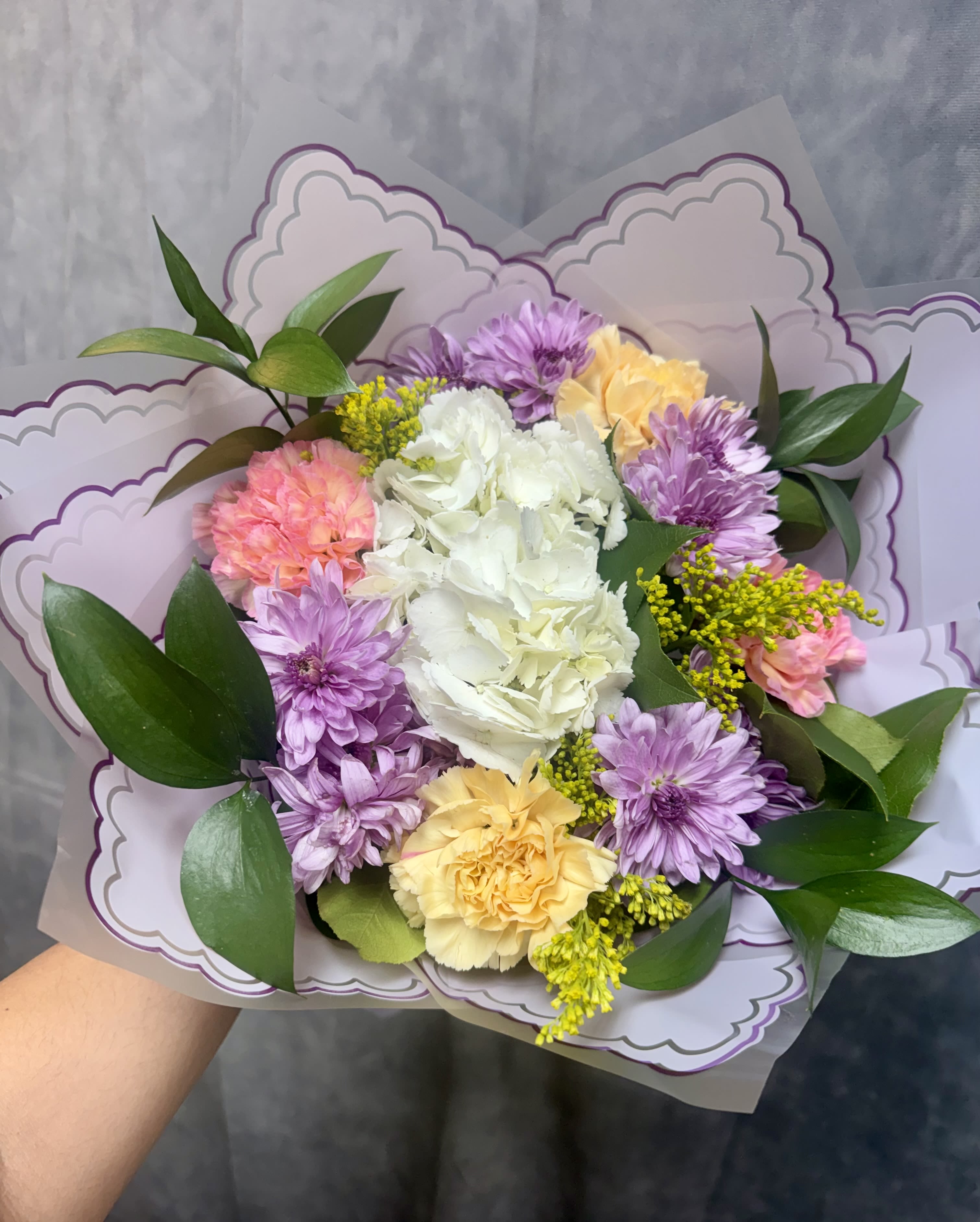 Lavender Cream Delight Bouquet  - A soft and elegant mix of lavender mums, creamy hydrangea, buttery yellow and blush carnations, accented with golden solidago and fresh greenery. This bouquet blends gentle pastel tones with natural garden charm, making it perfect for birthdays, get well wishes, thank you gifts, or simply brightening someone’s day.  Fresh, graceful, and full of warmth — a true delight in every bloom. 