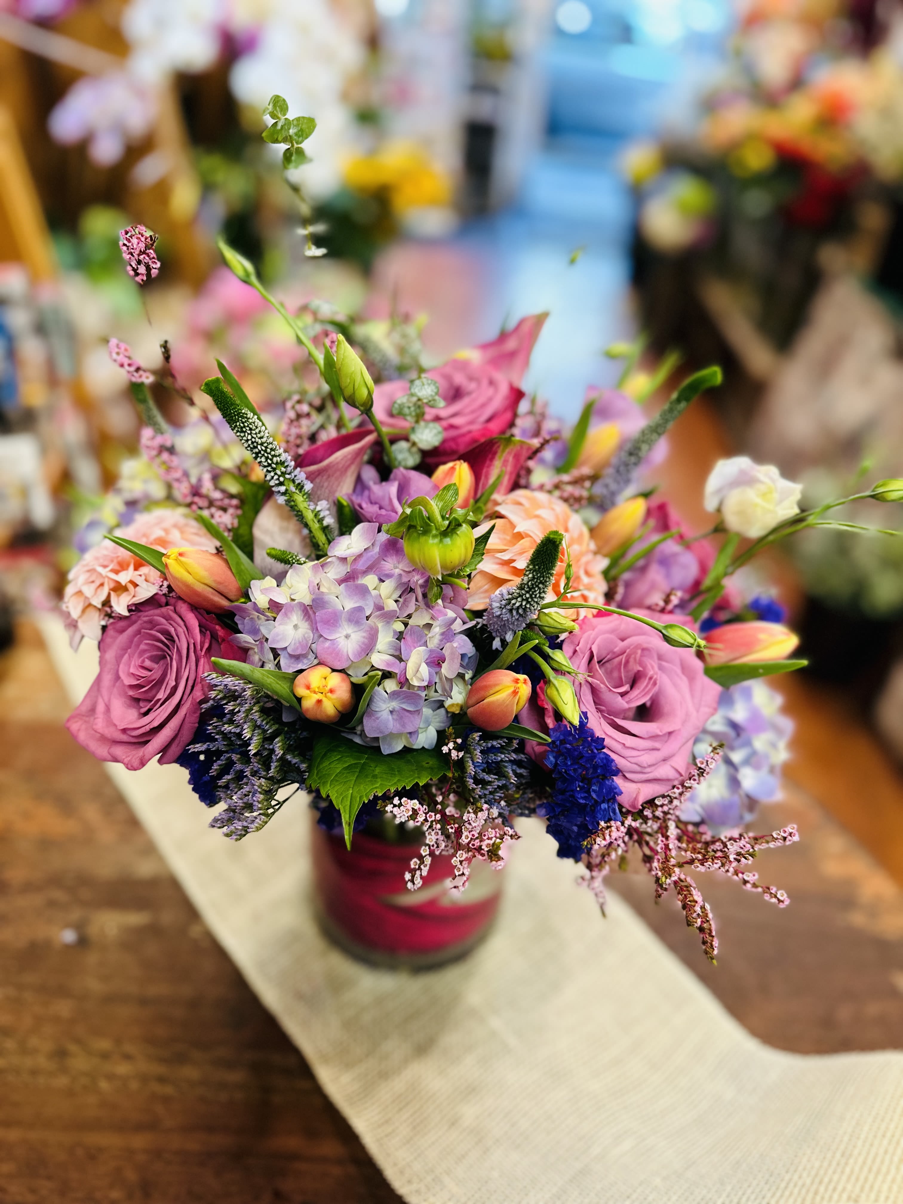 Unforgettable  - This lovely arrangement comes in a low cylinder vase with vibrant tulips, hydrangeas,  lavender roses, lisianthus,  stock, Bella Donna, statice, veronica and various greenery.  Some flowers may be subject to change depending on the season. We will contact you with available flower substitutions; please contact us with specific questions if you are concerned with flower availability, thanks! Featured arrangement is $135.75