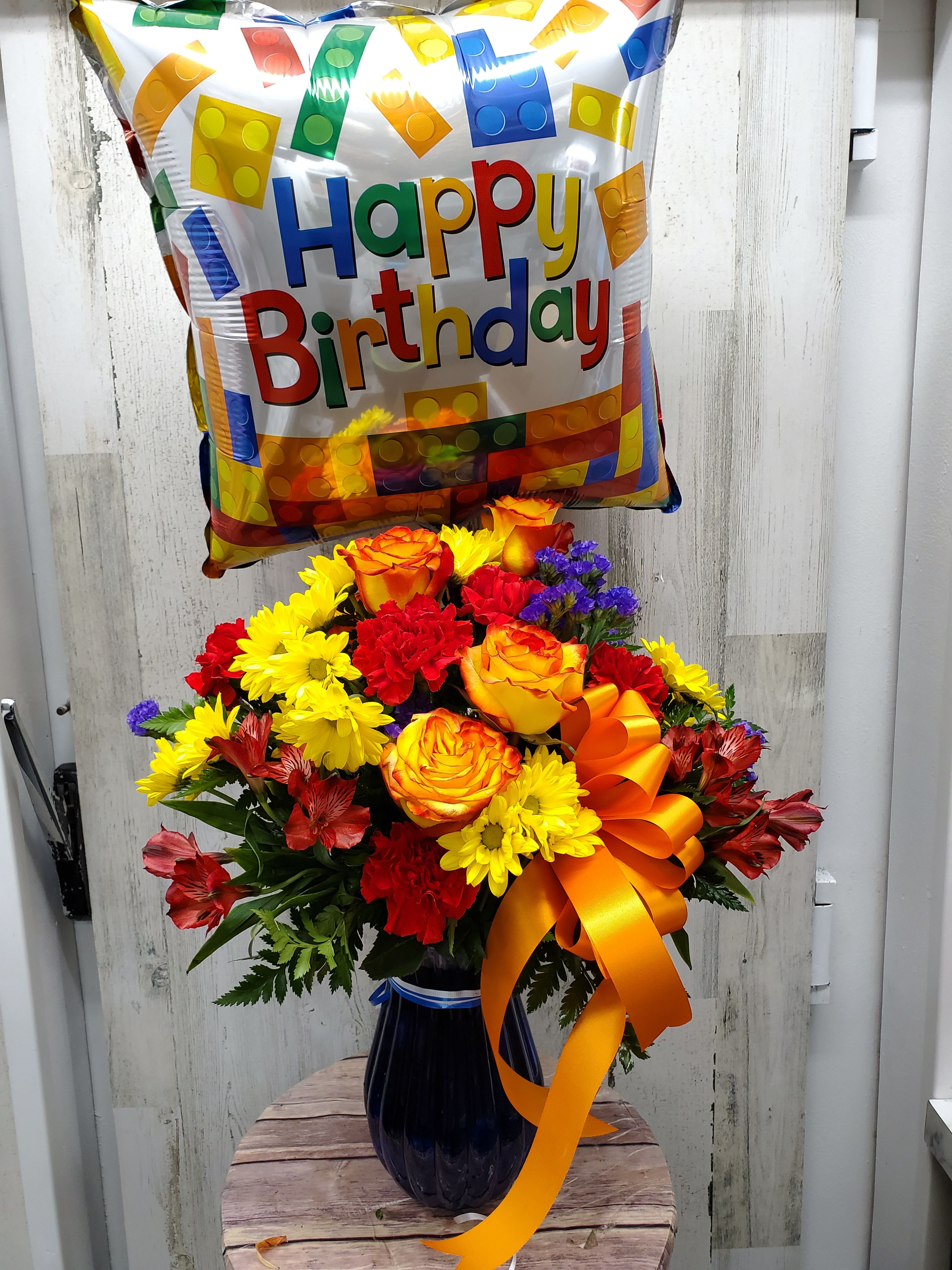  Tabitha - Brilliant orange roses, yellow alstroemeria, red carnations and miniature carnations, yellow daisy spray chrysanthemums, purple statice and a big bright balloon are all delivered in a beautiful cobalt blue vase. It's a thumbs-way-up choice in birthday gifts!   