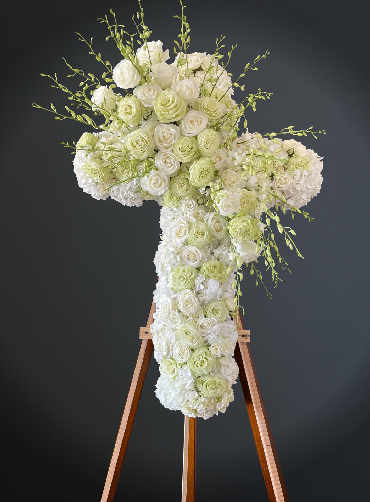 Eternal life and love - This graceful standing cross, artfully designed in the shape of a cross, features an exquisite blend of soft white and ivory roses, hydrangeas, and delicate orchids. Accented with subtle green blooms and sprigs, this arrangement offers a serene and heartfelt expression of peace, faith, and remembrance. Perfect for memorial services, funerals, or a tribute of deep spiritual significance, this floral cross stands as a beautiful symbol of eternal life and love.