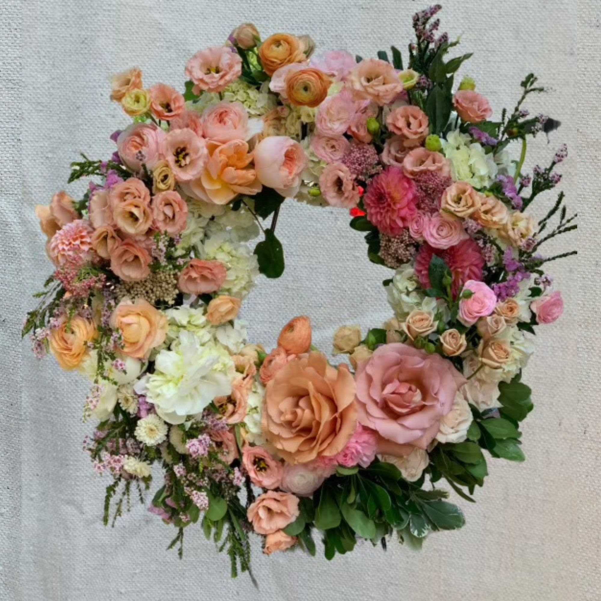 Sweet Reminiscence - A breathtaking garden wreath overflowing with romantic blooms in soft peach, blush pink, lavender, and cream tones. This luxurious tribute features an abundant mix of garden roses, ranunculus, lisianthus, dahlias, spray roses, hydrangea, waxflower, rice flower, and lush greenery, creating an unforgettable expression of love, beauty, and cherished memories.  Specific florals can be included or removed and colored themes are available. Each wreath includes a 5' wire easel and is expertly crafted with the freshest blooms and greenery.