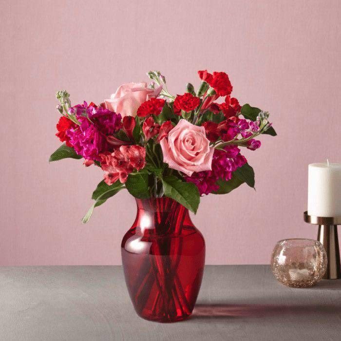 Cupid's Crush - Ignite romance with Cupid’s Crush, a breathtaking floral arrangement designed to captivate hearts. This passionate bouquet features a luxurious blend of soft blush pink roses, bold red carnations, and rich fuchsia blooms, creating a striking balance of romance and elegance.  Arranged in a deep ruby-red glass vase, this bouquet exudes warmth, passion, and timeless beauty. The lush greenery adds depth and contrast, enhancing the vibrancy of the flowers. Perfect for Valentine’s Day, anniversaries, or simply to say ‘I love you’, this arrangement is a stunning symbol of affection and devotion.  Let Cupid’s Crush speak the language of love—because nothing says romance like fresh, exquisite blooms. 