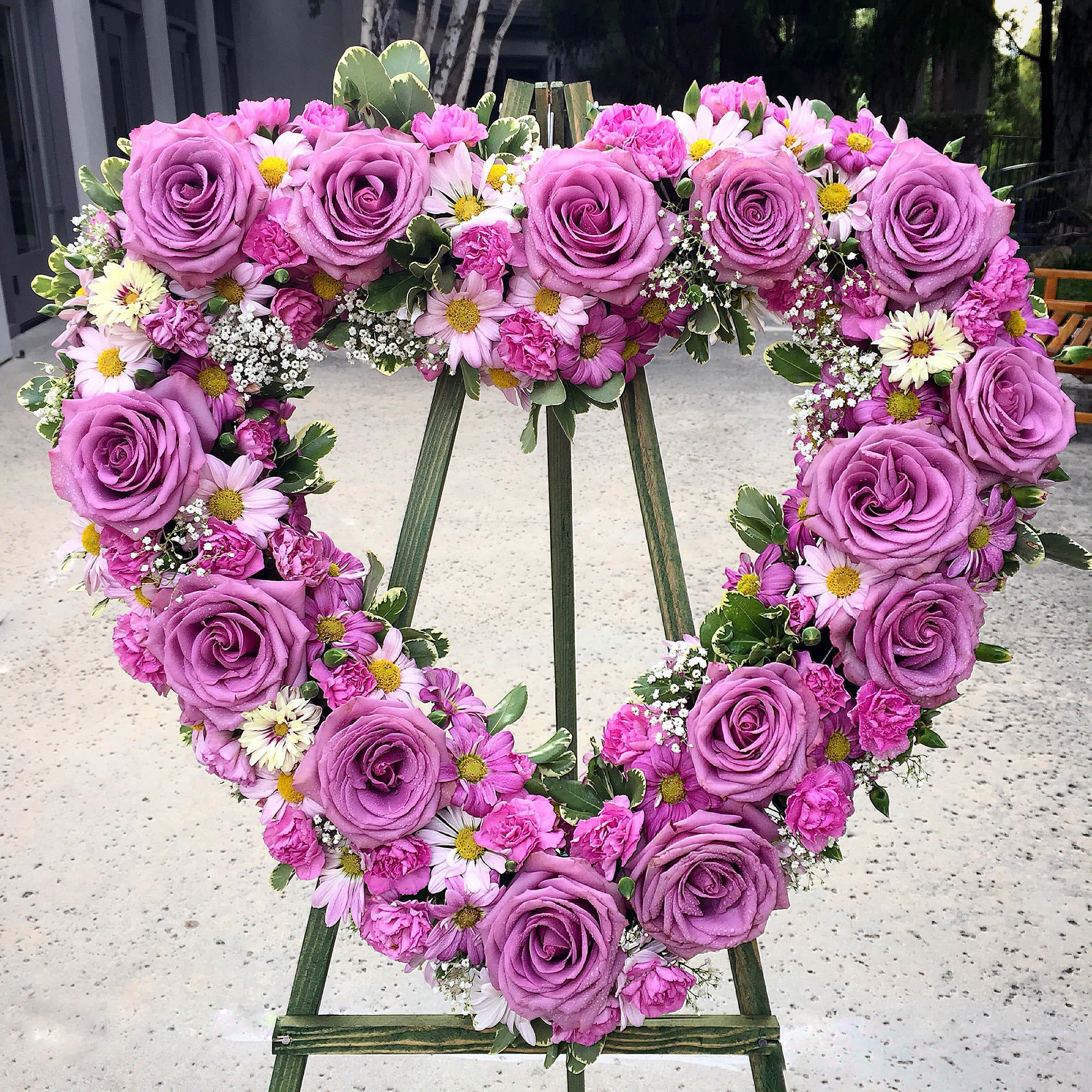 Grieving Heart Standing Wreath - When your heart is grieving over the loss of a loved one or just want to send your sympathies to a family or friend, this heart shaped wreath beautifully arranged with all lavender roses, daisies, carnations and baby's breath will be the utmost appropriate to commemorate this occasion. Give some comfort and express love to yourself, your family and everyone through these lovely flowers.   Approximately 22" D 