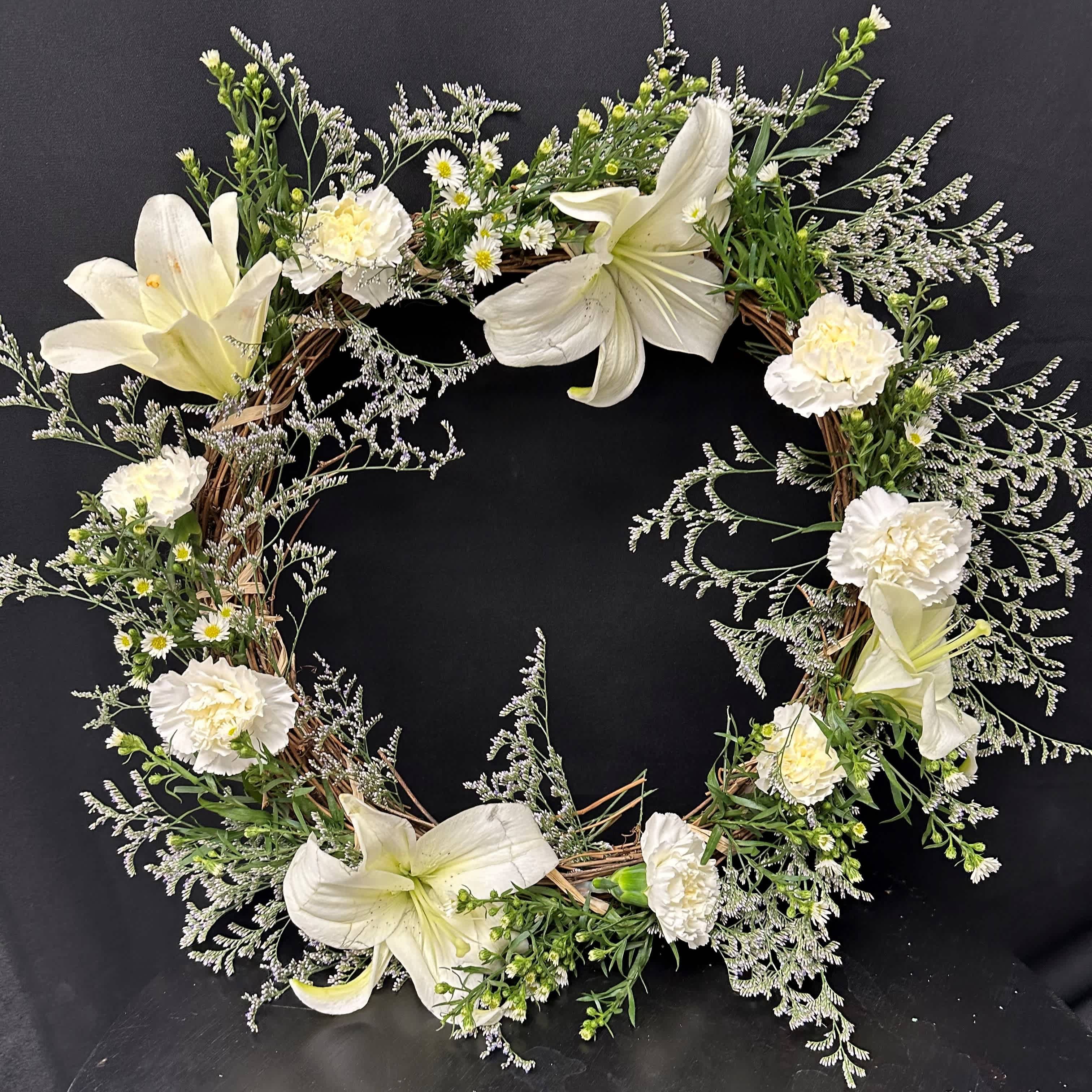 White floral wreath with lilies and carnations on a dark background