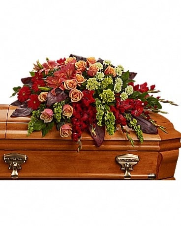 A Fond Farewell Casket Spray - An overflowing of love and respect is joyfully expressed in this truly magnificent casket spray of orange roses and lilies and other brilliant blooms. The magnificent arrangement includes green miniature hydrangea, orange roses, dark orange asiatic lilies, red gerberas, red gladioli, green carnations and bells of Ireland, accented with assorted greenery.Approximately 44" W x 25" H