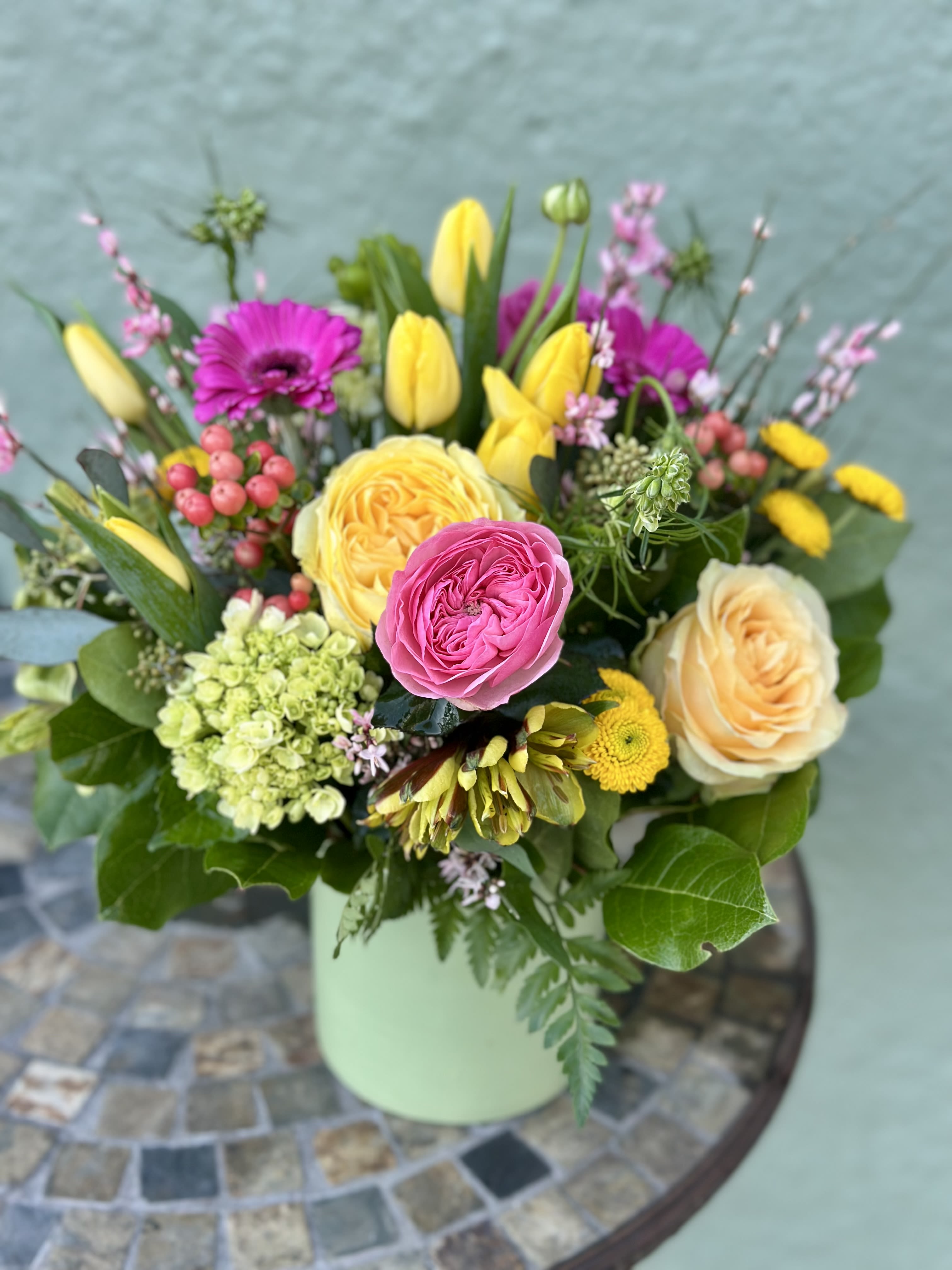 Your Song - Celebrate a love that deserves its own anthem with "Your Song". This vibrant and joyful arrangement features a harmonious melody of sunny yellow roses and tulips, symbolizing friendship, happiness, and perfect love. These cheerful blooms are beautifully complemented by pink roses and gerbera daisies, which express admiration, appreciation, and pure affection. Accented with lush green hydrangeas for growth and renewal, "Your Song" is the perfect way to express the depth of your feelings.