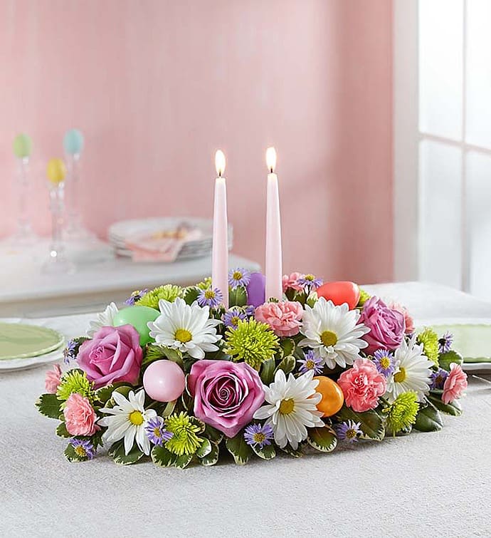 Easter Flower Centerpiece With Candles - When family and friends gather at the holiday table, all eyes will be on our charming centerpiece. A handcrafted mix of soft pastel blooms is accented with colorful Easter eggs for a playful touch. Topped off with elegant taper candles, it’s a lovely way to share holiday smiles.