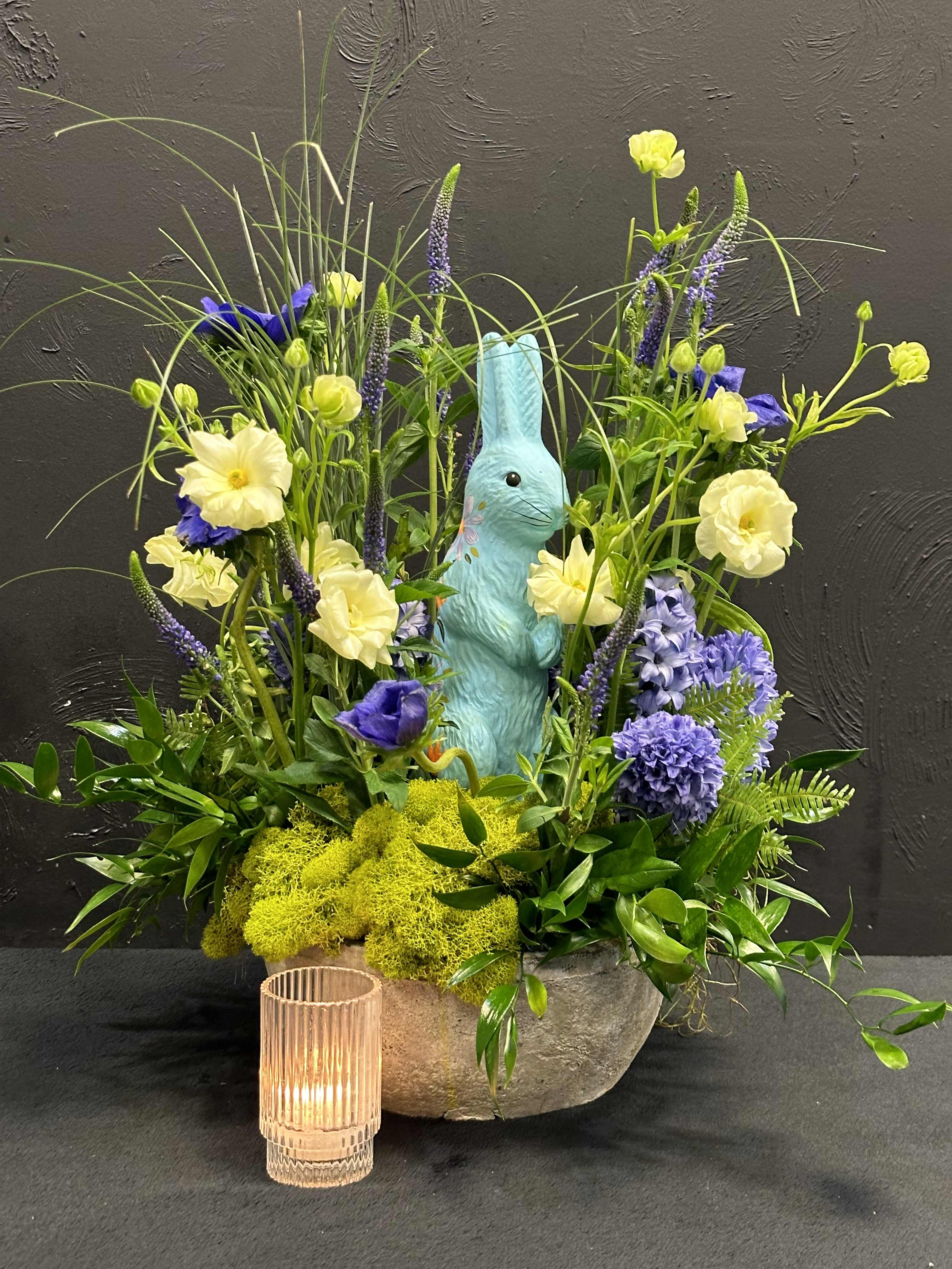 Blooms by Blue Bunny - The Blue Bunny arrangement is a delightful composition of fresh blooms, This exquisite creation features the ethereal allure of buttercream Japanese ranunculus, their soft petals unfurling like whispers of spring. Paired with the intoxicating fragrance of hyacinths, each bloom a fragrant note in nature's symphony. The arrangement is housed in a rustic stone vase, adding an earthy touch to the overall presentation.