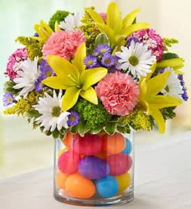 EASTER EGG CENTERPIECE - Make their Easter egg hunt an extravaganza of smiles! Our truly original arrangement of pastel lilies, carnations and more is handcrafted inside a glass cylinder vase filled with colorful plastic eggs. Whether it’s adding a playful touch to the holiday table or sent as a surprise for “somebunny” special, this playful bouquet was designed for fun.