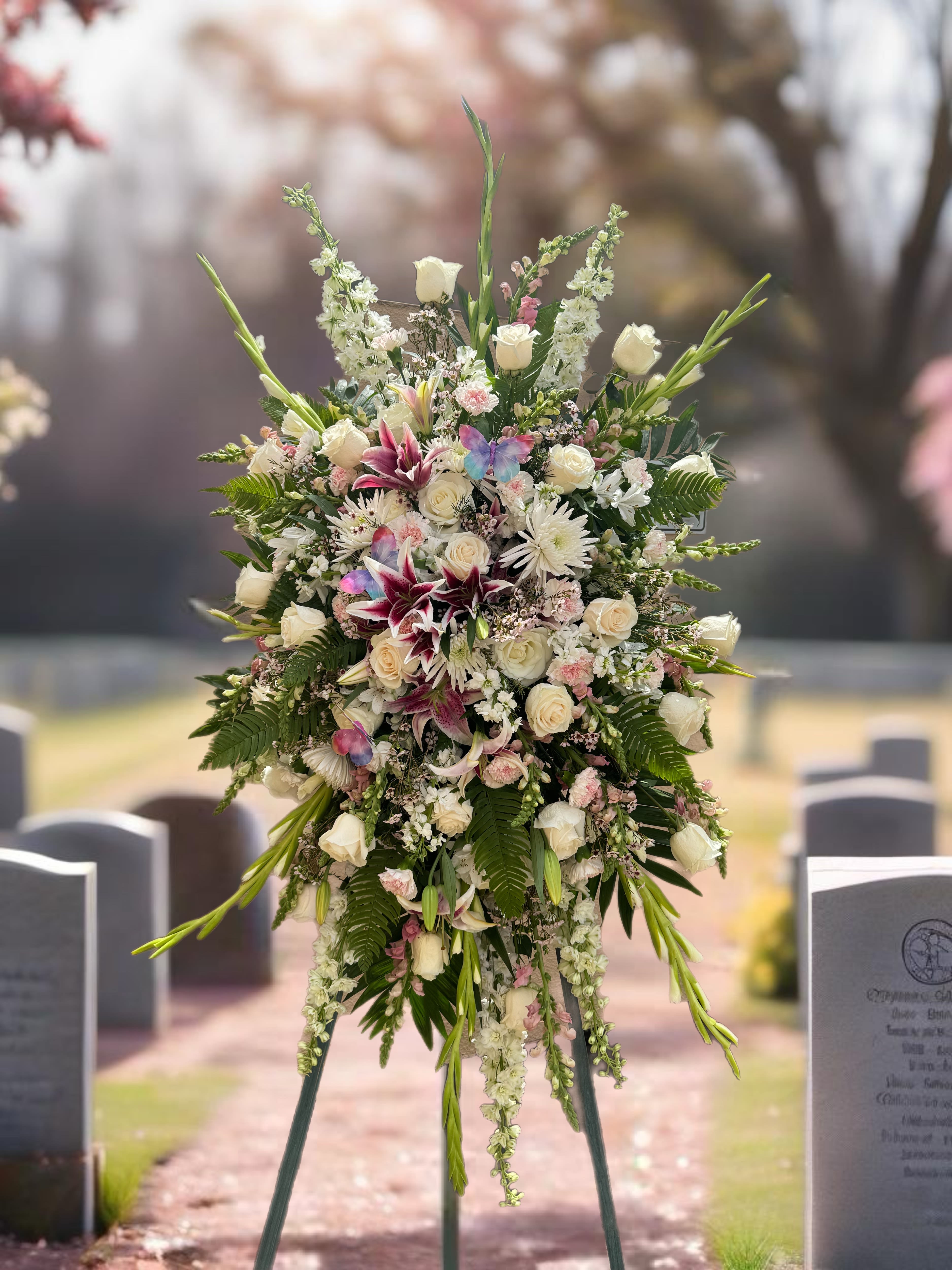 Butterfly Bloom - "Butterfly Bloom" is a vibrant, enchanting arrangement of roses, stargazers, larkspur, gladiolus, stock, and more. The soft pink and white tones, paired with the beauty of the flowers, symbolize grace, transformation, and the lightness of a butterfly's wings - a tribute to a lively, spirited soul.  