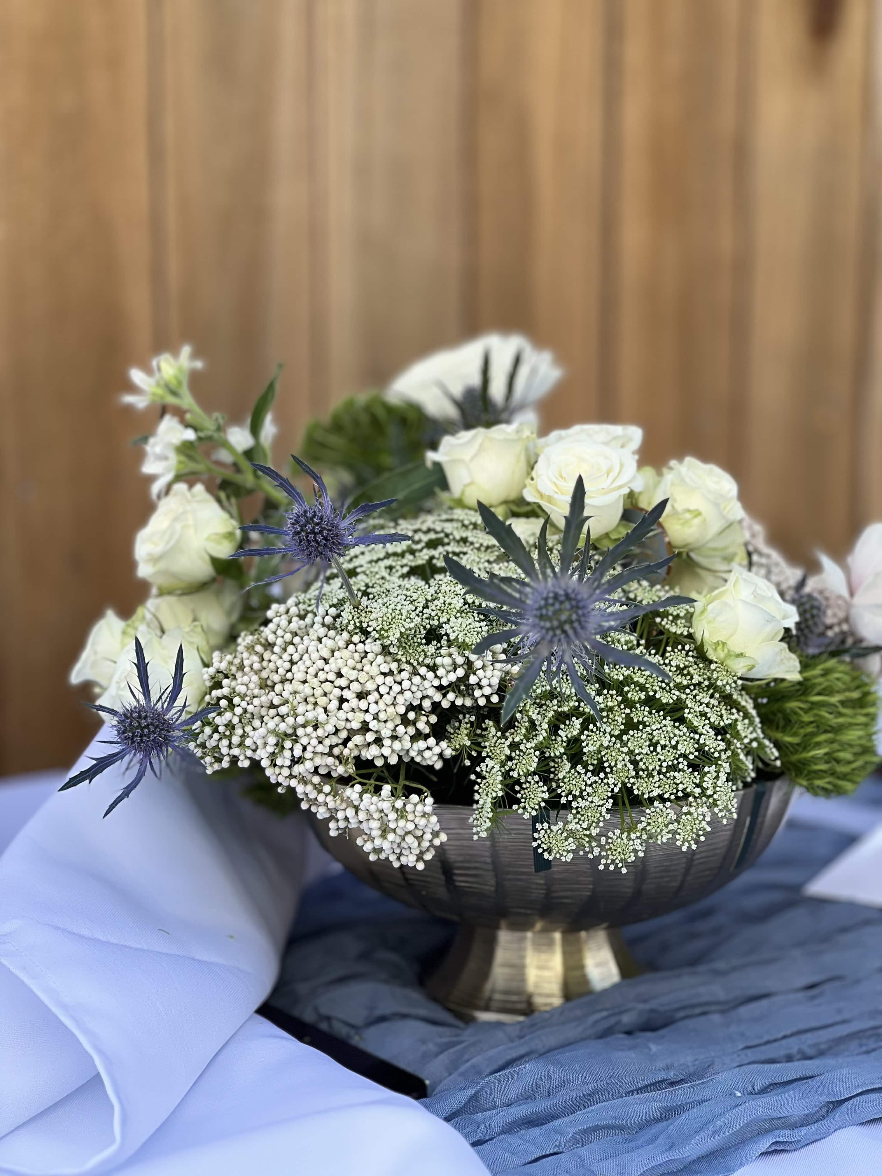 Fleur Mystique - Set in a lovely golden compote, a gentle composition of pink Baronesse roses, white spry roses ranunculus, Queen Ann's lace, thistle, hydrangea and a variety of white and blush flowers.   As with all our arrangements ~ we select the best, freshest and in season florals. This composition is a an inspiration, and what will be created for you is similar, but not exactly the same.  We do however promise that it will be equally as stunning as the composition in this image