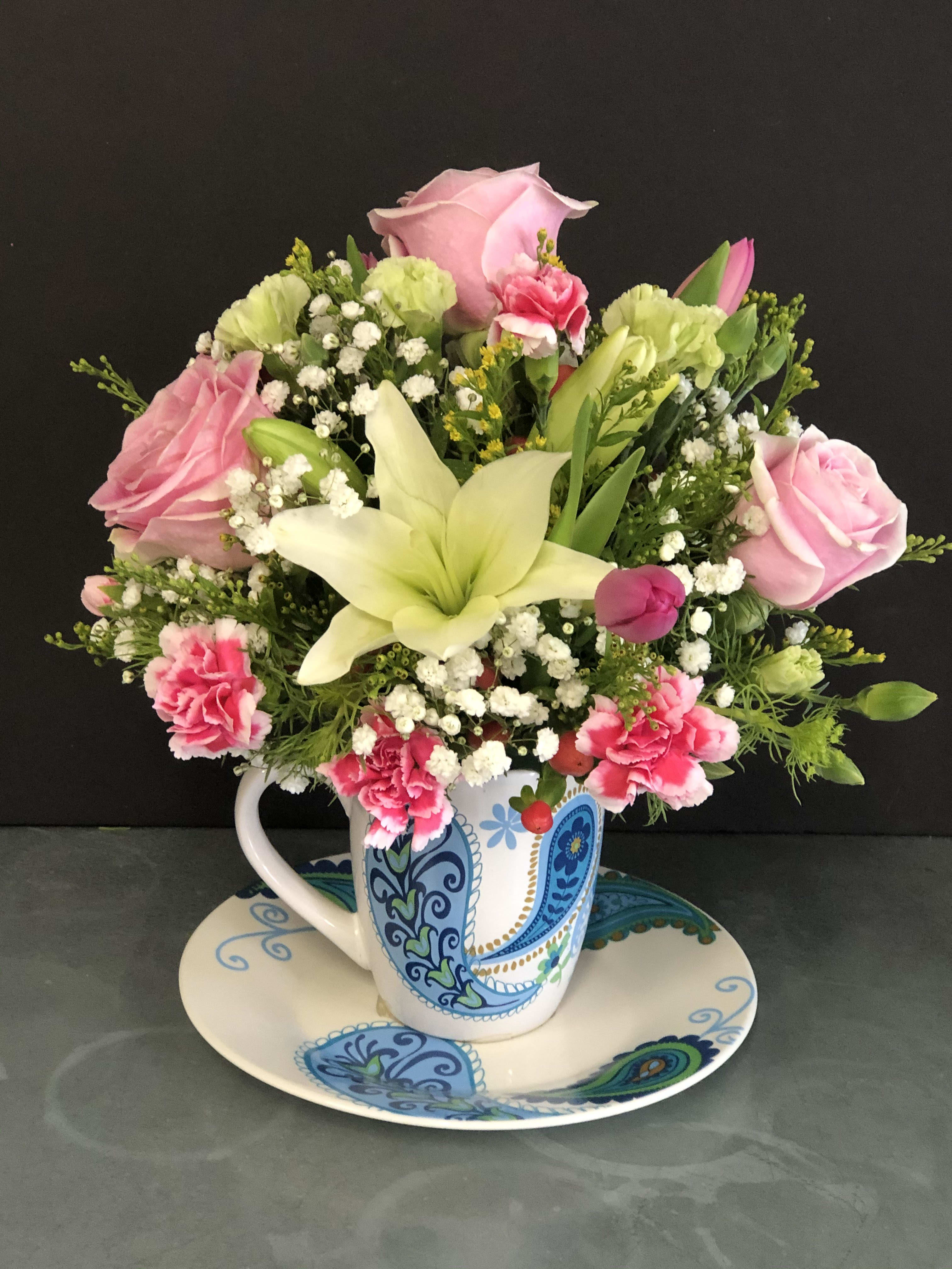 Pink roses and lilies arranged in a patterned mug on a matching saucer