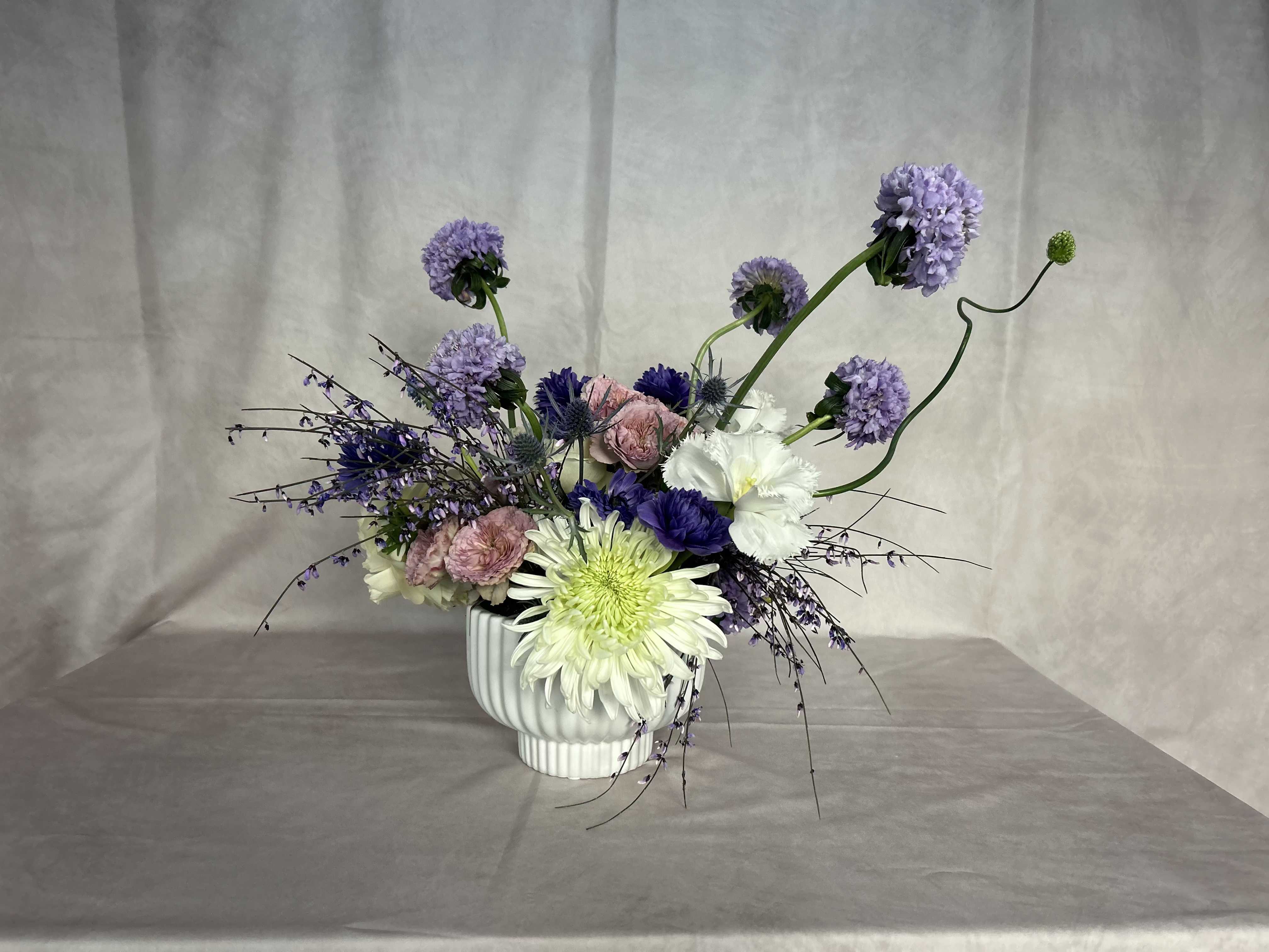Opal Blossom - Purple and lavender blooms stand out and create a lasting impact! A combination of Alliums, Agapanthus, mums, roses and anthuriums Set in a lovely ceramic modern vessel This arrangement is sure to delight and bring joy!  As with all our arrangements ~ we select the best, freshest and in season florals. This composition is a an inspiration, and what will be created for you is similar, but not exactly the same.  We do however promise that it will be equally as stunning as the composition in this image
