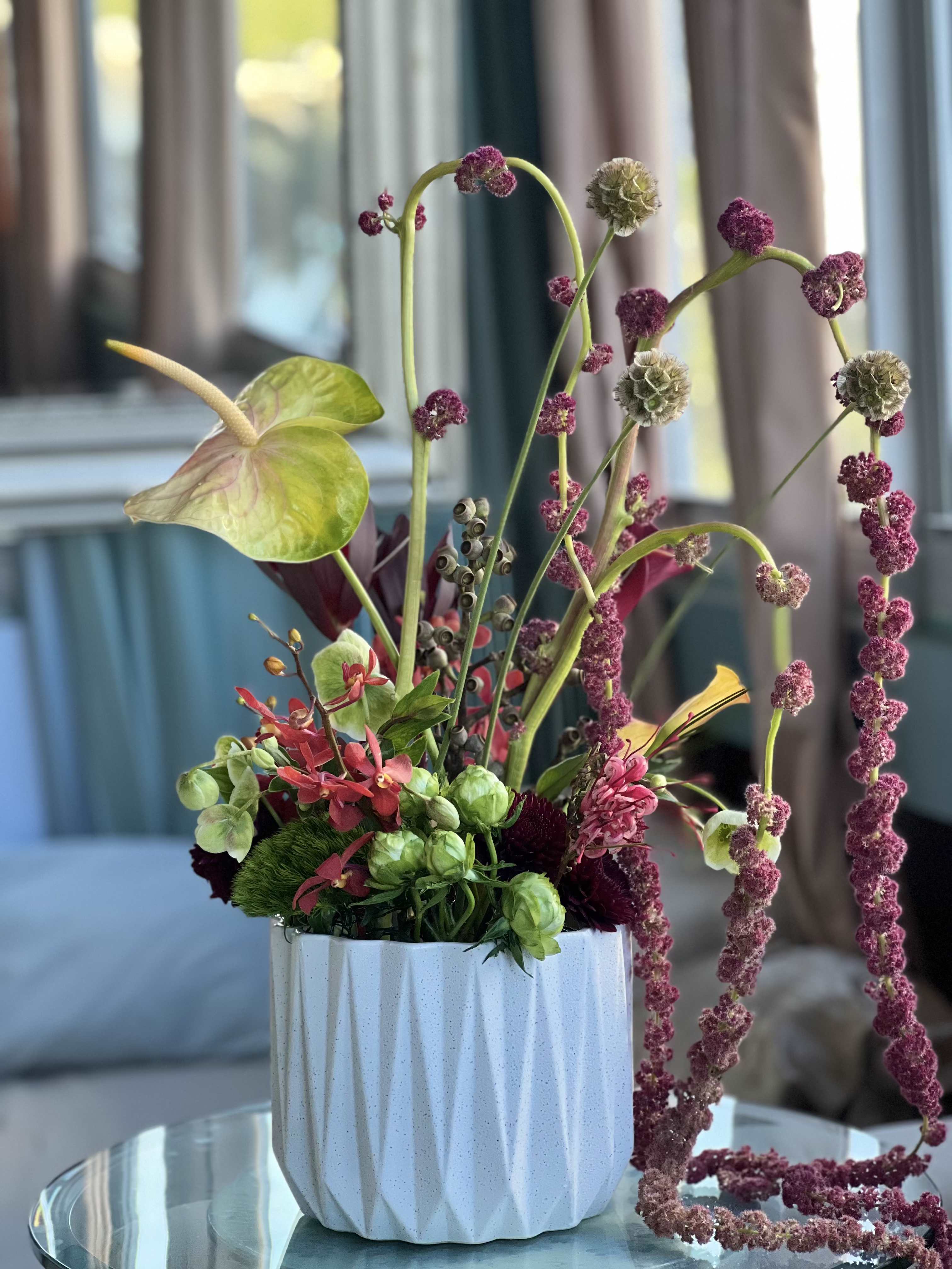 Heightened Muse - Amaranthus add height, greens add texture, roses add layers, and anthurium adds even more interest to this stunning arrangement set in a lovely white ceramic vessel 