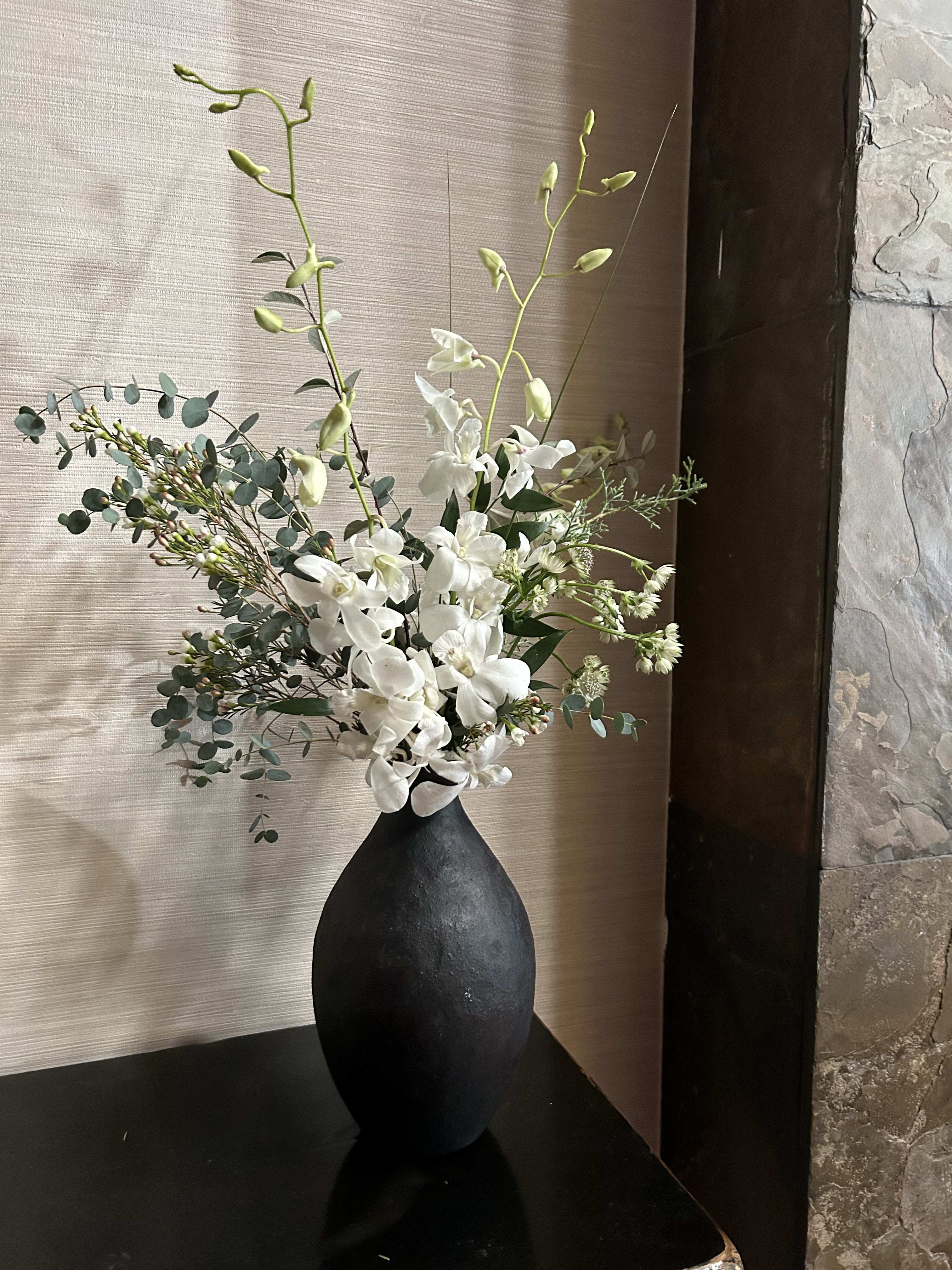 Jardin Blanc - Simple, elegant, unique. Ample orchids, greens, eucalyptus set in a unique black vessel