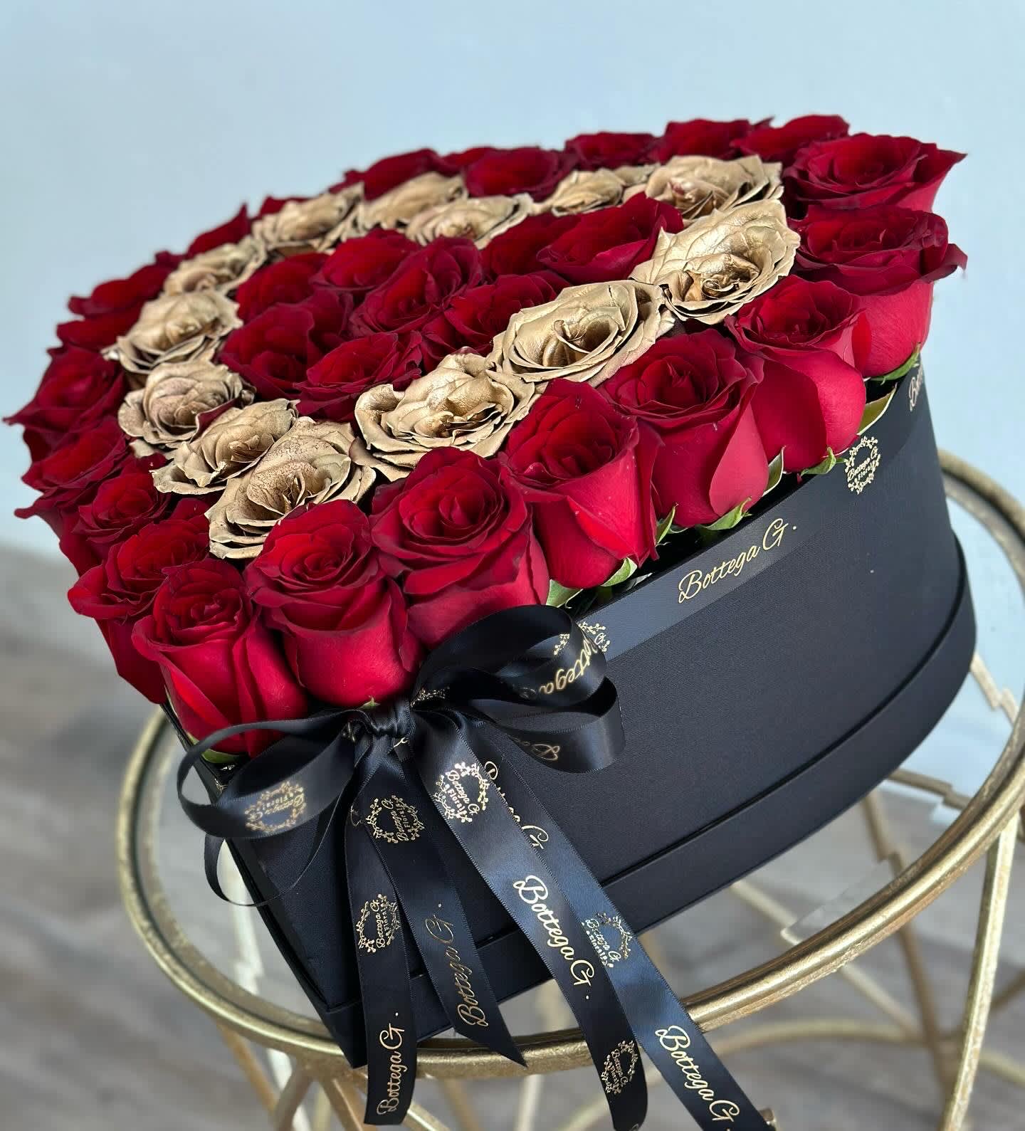 Red &amp; Gold Rose Heart Box - Immerse yourself in the language of love with our "Red &amp; Gold Rose Heart Box" — a captivating arrangement that transforms passion into a visual masterpiece. Nestled within a heart-shaped box, this ensemble features a sumptuous collection of Bottega's specialty gold roses, meticulously arranged to ignite the flames of romance.  The deep, velvety red roses, symbolizing enduring love, are carefully selected to convey the intensity of your emotions. Each petal unfolds like a love letter, creating an enchanting mosaic within the heart-shaped box. This meticulously crafted arrangement is a celebration of love's timeless beauty and the profound connection between hearts.