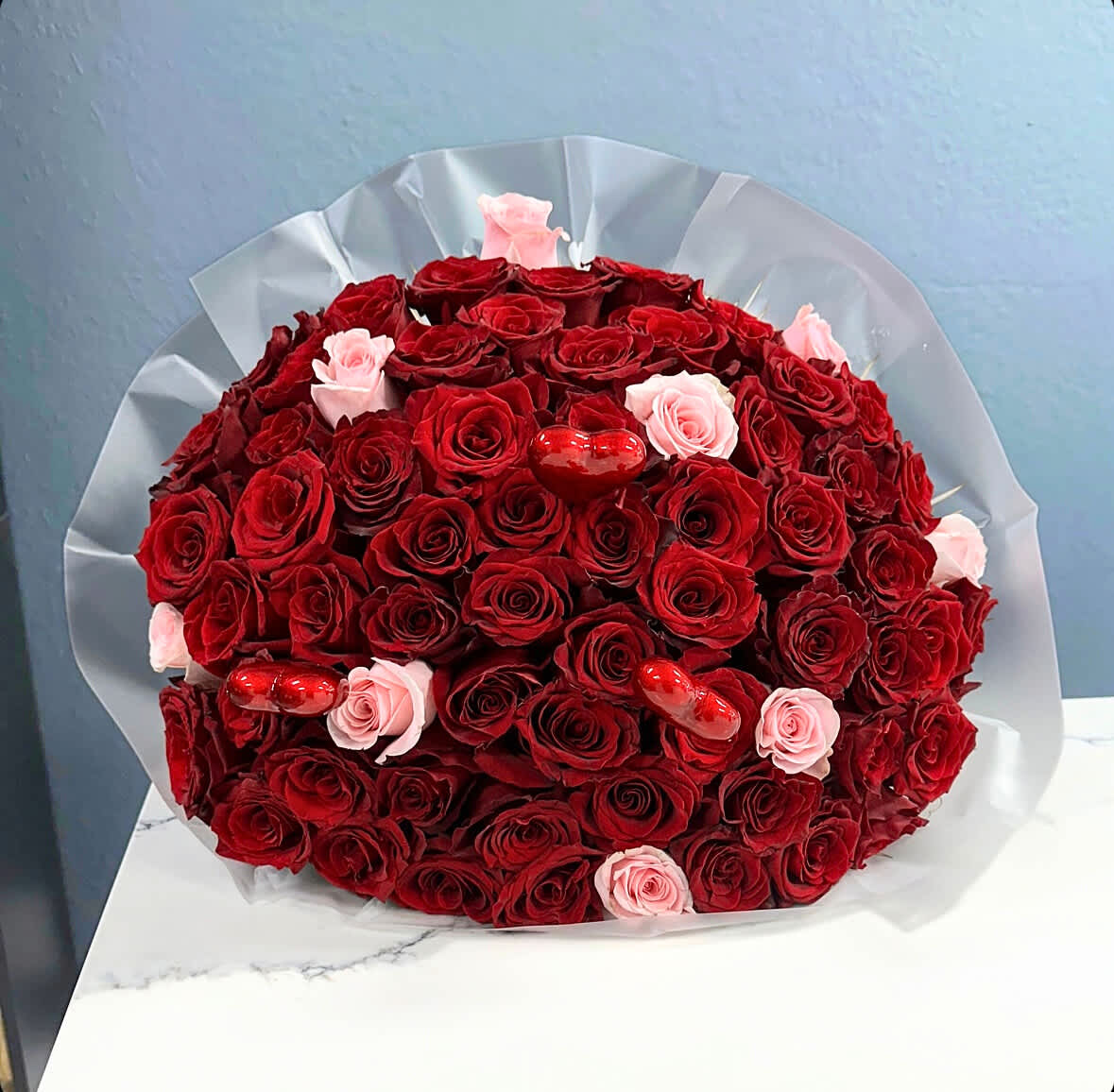 Forever &amp; Always Bouquet - Indulge in the romance of "Forever &amp; Always," a stunning Valentine's Day bouquet that artfully combines the timeless passion of deep red roses with the soft allure of subtle pink roses, all crowned with delicate heart accents. This arrangement is a celebration of love's many hues, encapsulating the warmth and tenderness that make this day so special.  The rich, velvety red roses stand as a symbol of deep love and desire, while the gentle blush of the pink roses adds a touch of sweetness and sophistication. Together, they create a harmonious blend that speaks to the depth and beauty of your connection.  To add a whimsical touch, the bouquet is adorned with enchanting heart-shaped accents.