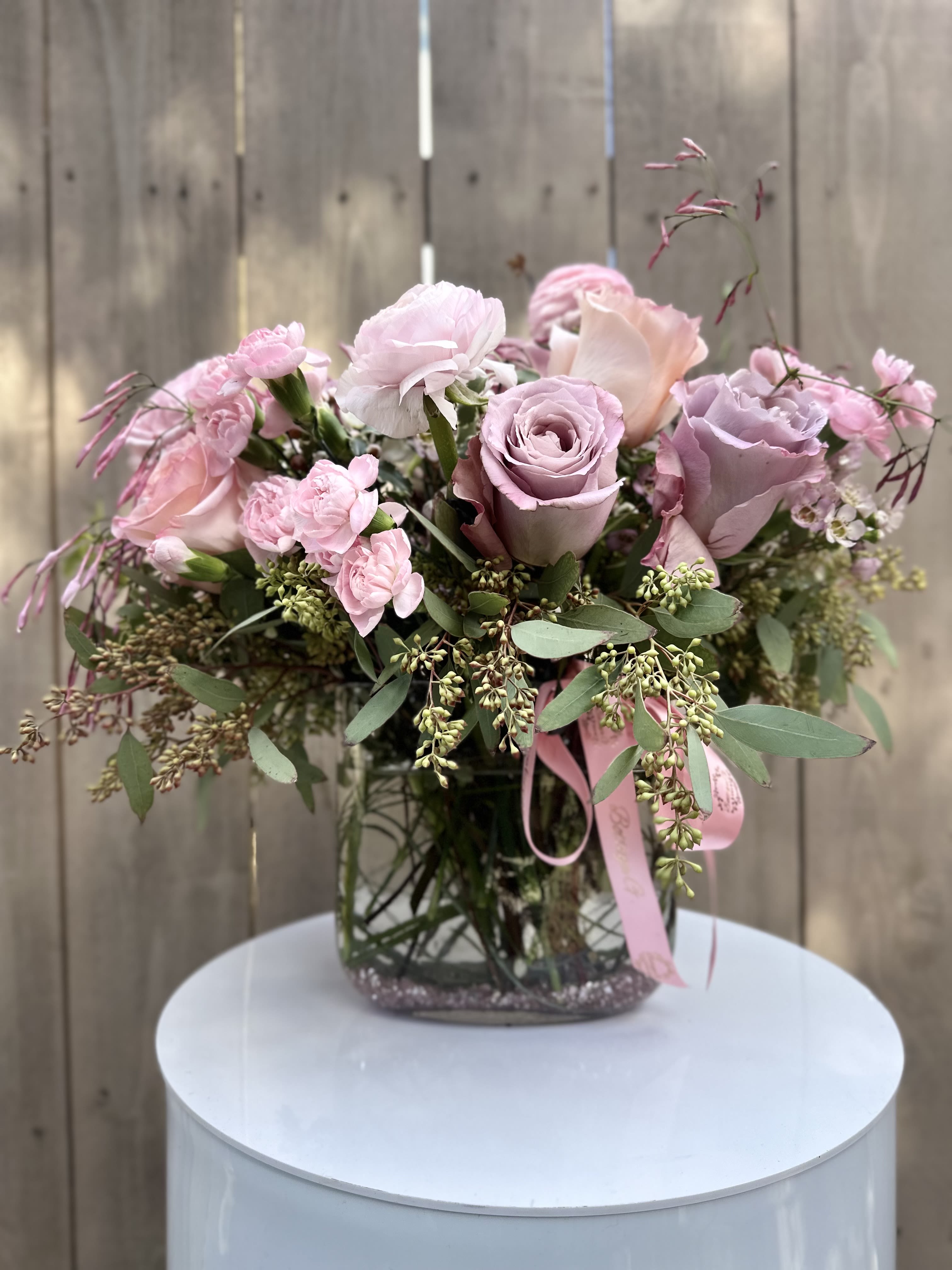 Lavender Lagoon - A charming arrangement of light purple roses displayed in a clear glass fishbowl vase. The roses, with their soft lavender petals, radiate elegance and serenity, while their lush green stems are fully visible through the transparent glass. 