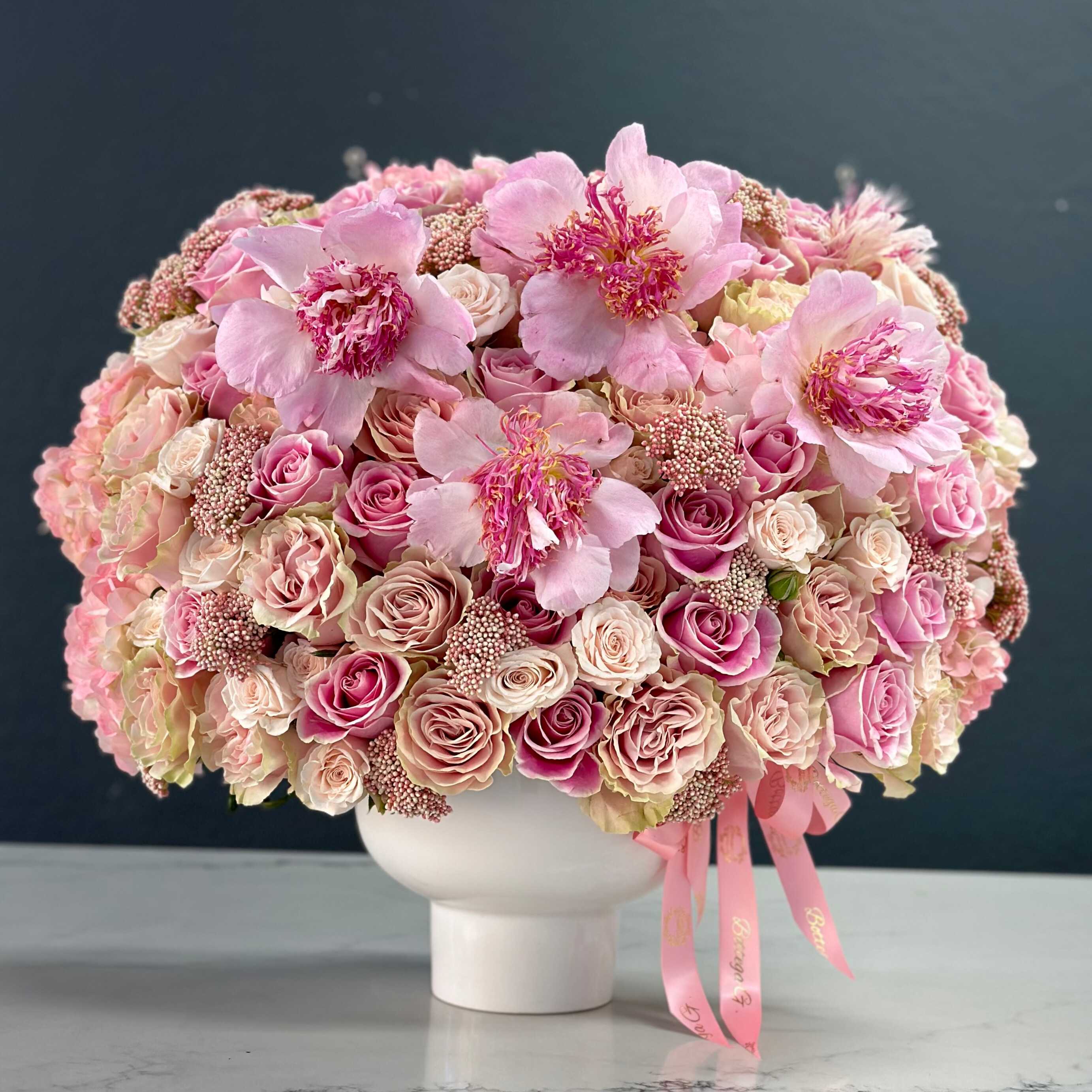 Sweet Serenade - This exquisite arrangement is a celebration of maternal love and tenderness, designed to evoke heartfelt emotions with its soft, pink hues and graceful blooms.  At its center, a lush bouquet of pastel pink roses takes pride of place, symbolizing admiration, gratitude, and affection. Each velvety petal whispers a message of love, making it a perfect tribute to the nurturing spirit of mothers everywhere.  Complementing the roses are clusters of delicate pink carnations, their gentle fragrance infusing the air with a sense of tranquility and joy. These blooms represent admiration and gratitude, reflecting the beauty and strength found in maternal bonds.