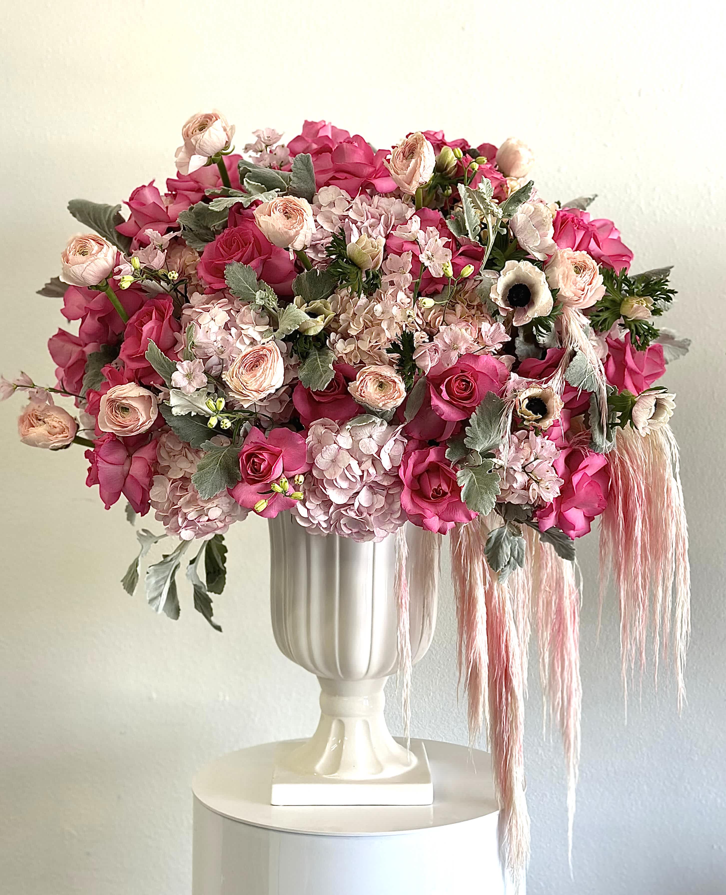 Chic Charm - This stunning arrangement combines the delicate beauty of anemones, the lush texture of ranunculus, the classic elegance of roses, and the voluminous charm of hydrangeas. These exquisite blooms are thoughtfully arranged in a tall, sleek white vase, creating a striking centerpiece that exudes grace and refinement.   Flowers Included:  Anemones: Known for their striking appearance, these flowers add a touch of whimsy and elegance. Ranunculus: Their layered petals bring a lush, romantic feel to the arrangement. Hydrangeas: These voluminous blooms add texture and depth. Roses: A symbol of love and beauty, they bring timeless elegance to the bouquet.