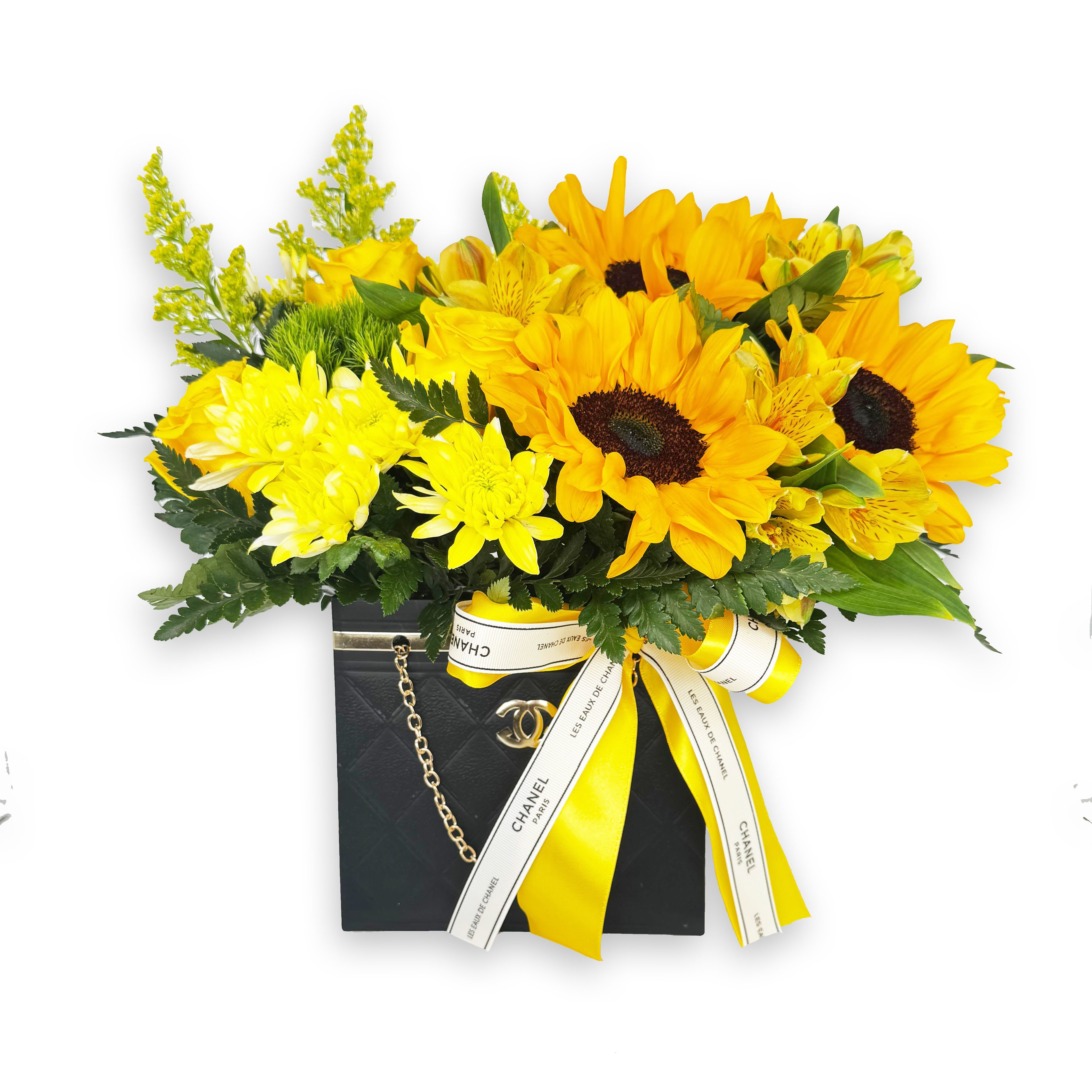She Blooms Beautifully - A radiant sunflower arrangement designed inside an elegant Chanel-inspired keepsake bag, blending timeless style with vibrant charm. Featuring fresh, golden sunflowers paired with lush greenery and delicate accent blooms, this design captures warmth, confidence, and effortless beauty.  Perfect for celebrating strong, stylish women, birthdays, Women’s Day, or just because — this arrangement makes a statement the moment it walks into the room.