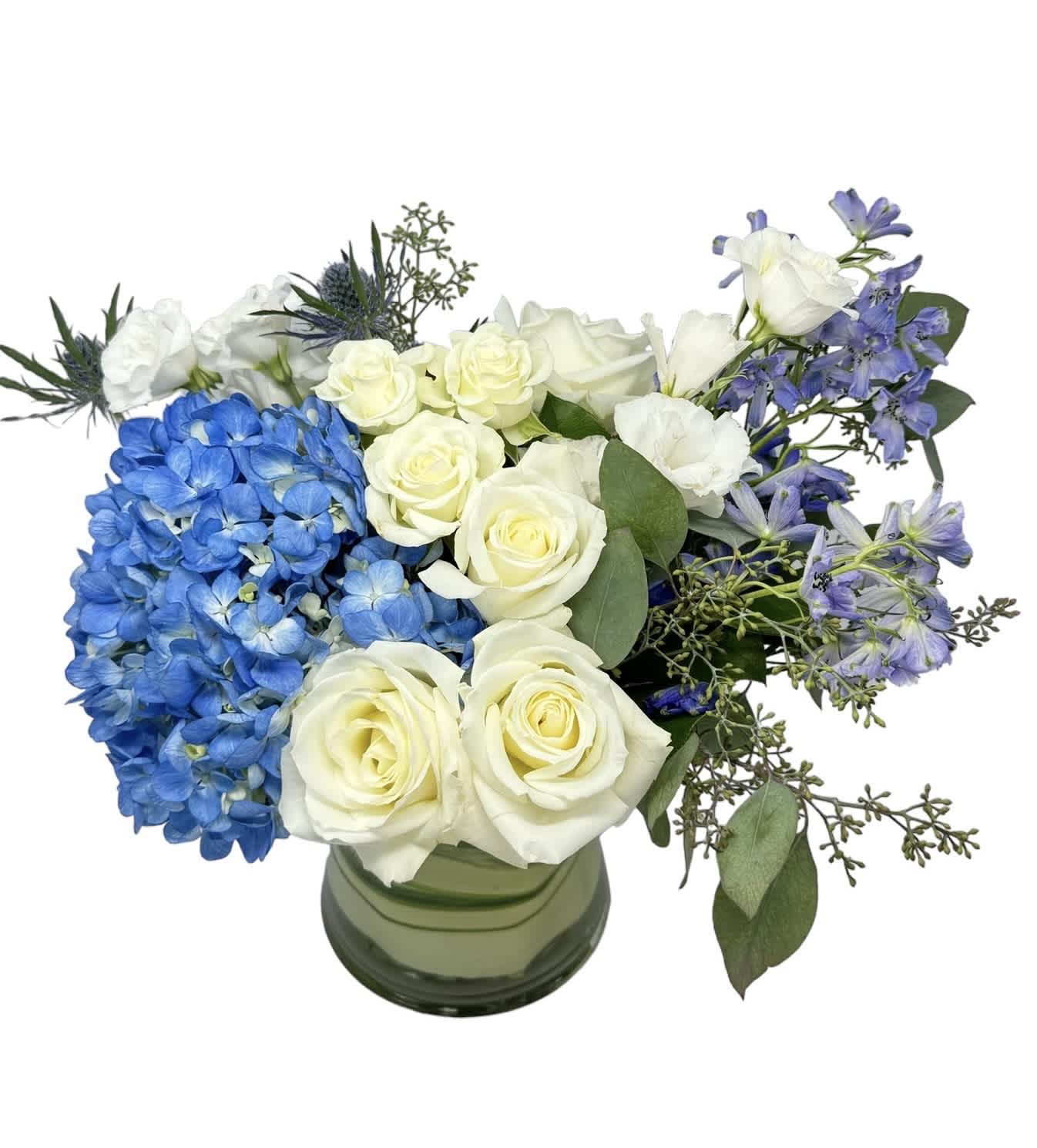 Nantucket Beach - Blue hydrangea, white roses, white spray roses, blue delphinium, blue thistle and seeded eucalyptus designed in a glass vase. As shown in photo.