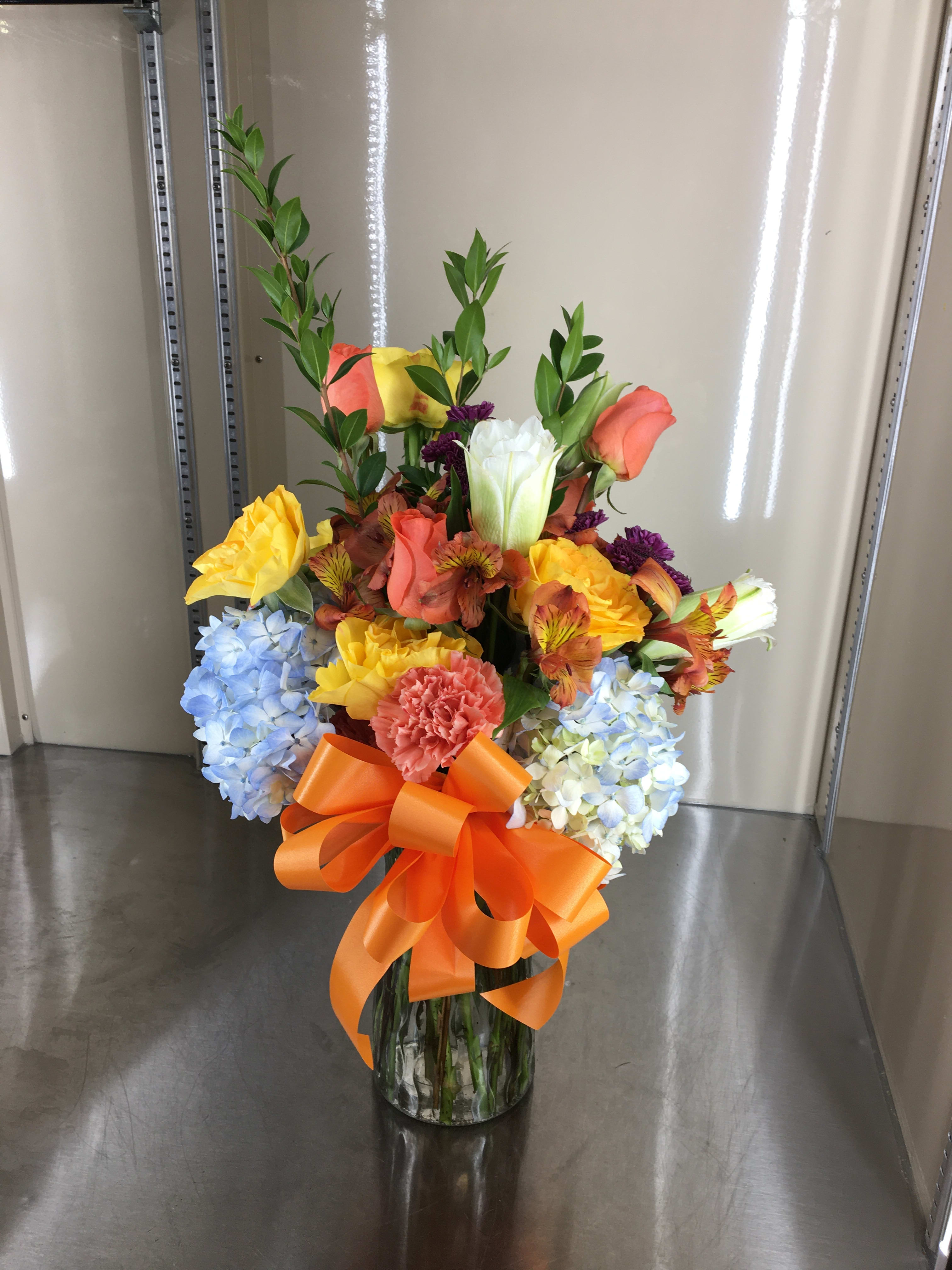 Ready to Go - Mixed cut arrangement with yellow roses, blue hydrangea, orange alstroemeria, salmon roses, and salmon carnations, and lilies in a vase 