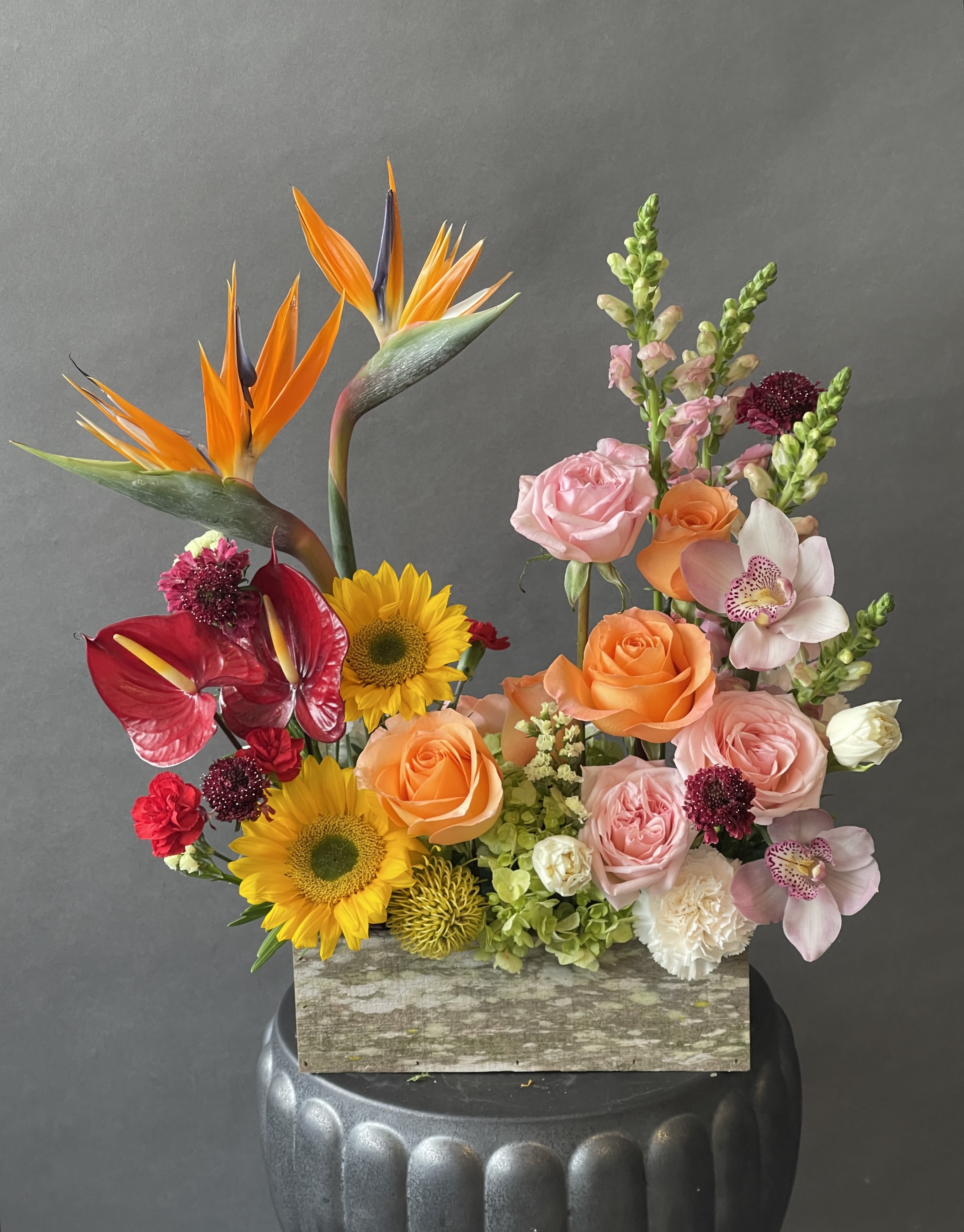 Mixed floral arrangement with sunflowers, roses, orchids, and bird-of-paradise in a wooden box