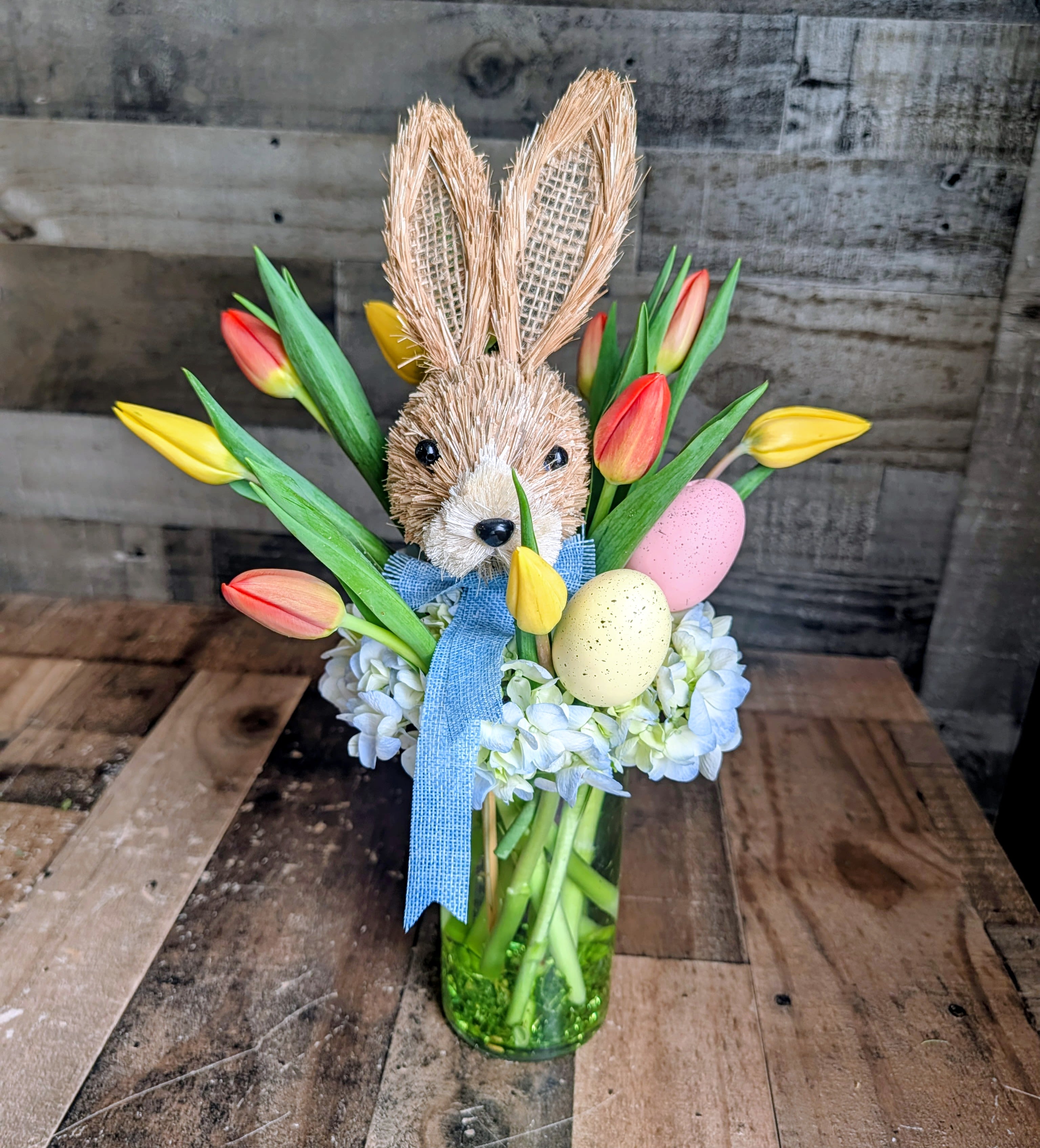 Hippity Hop Bouquet - Shown as Standard Hydrangea, tulips, a rabbit head and a couple colored eggs come designed in a cylinder with acrylic in the bottom. *We custom design this arrangement and use the freshest flowers available the day of delivery. The arrangement in this picture is an example of the size and style and may not feature the exact product shown.*