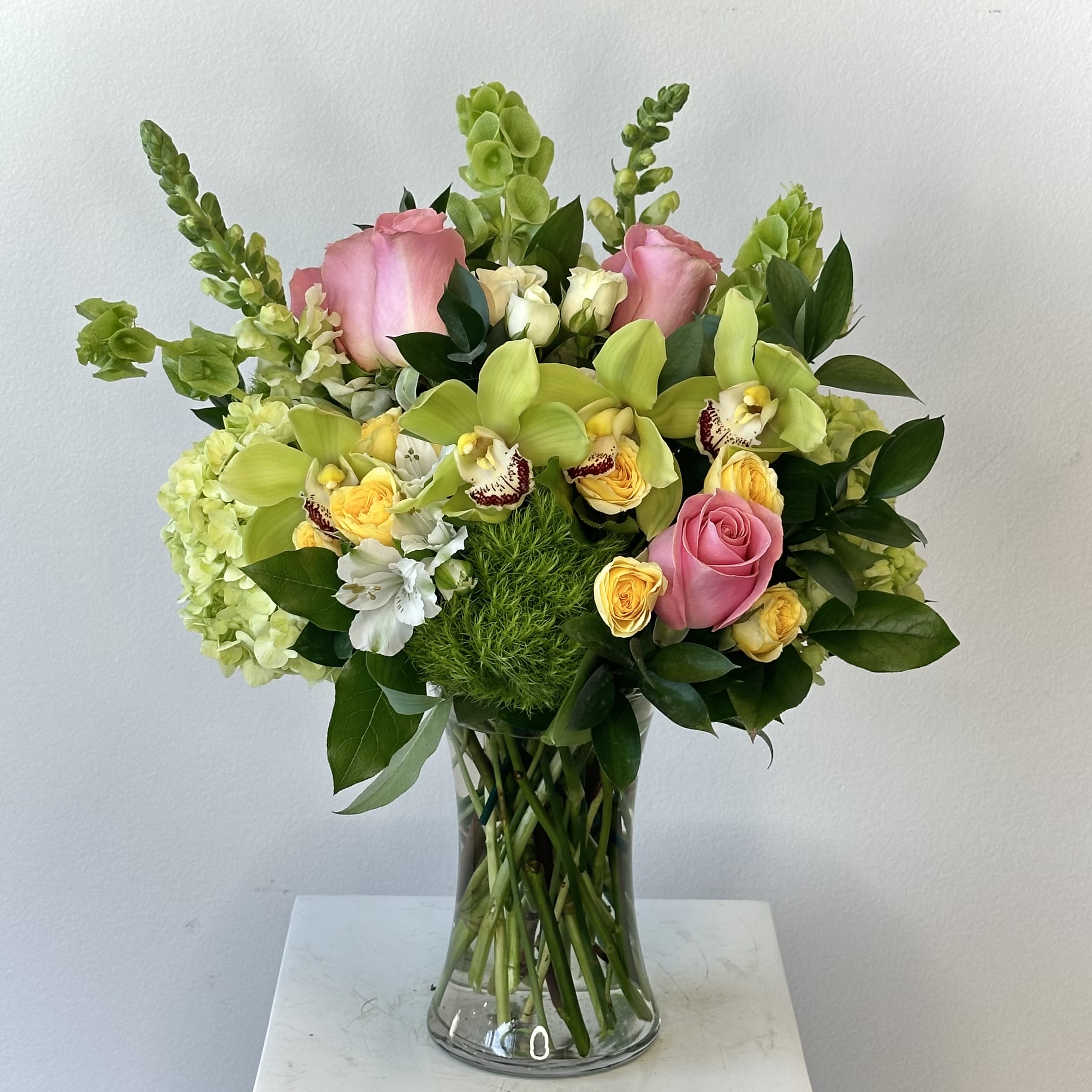 Pink Lemonade - Experience the refreshing beauty of the Pink Lemonade flower arrangement, a vibrant bouquet that captures the sweet, zesty essence of a cool glass of pink lemonade. With its lively blend of colors and textures, this stunning arrangement brings summer cheer and positivity to any setting. This delightful design showcases exotic green cymbidium orchids for lush, exotic appeal, romantic pink roses adding soft elegance and fragrance, tall bells of Ireland providing architectural green height and whimsy, charming dianthus balls for unique texture and color, sunny yellow and white spray roses for bright accents, graceful white snapdragons reaching upward with sophisticated lines, full lush green hydrangeas offering voluminous softness, and delicate white alstroemeria filling the arrangement with long-lasting starry blooms. The perfect pink and green flower arrangement creates a harmonious, eye-catching display that combines modern flair with classic beauty. Ideal as a birthday gift, anniversary flowers, Mother's Day bouquet, housewarming present, or beautiful home and office centerpiece, the Pink Lemonade arrangement is sure to delight recipients with its fresh, uplifting vibe. Hand-arranged by expert florists with premium, freshly cut flowers, each bouquet is unique. This customer-favorite floral design with orchids, roses, hydrangeas and more is the perfect way to express joy and celebration. Bring the zesty spirit of Pink Lemonade into your life now!