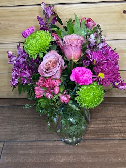 Blushing Garden Party - Blushing Garden Party is a lush, feminine arrangement filled with rich texture and playful color. Featuring soft pink roses, vibrant magenta daisies, bright green trick dianthus, and pops of hot pink carnation, this design feels both romantic and lively. Accented with snapdragons, alstroemeria, and fresh greenery, it’s arranged in a classic clear glass vase for a timeless finish.  Perfect for birthdays, anniversaries, or just because, this bouquet feels like a cheerful garden gathering captured in a vase — full of charm, color, and personality.