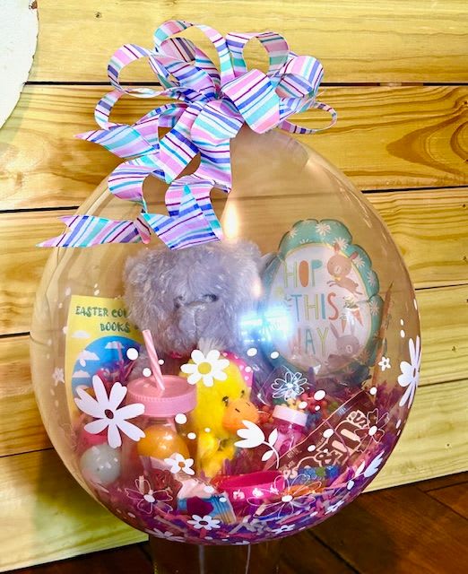 Sweet Surprise Bubble - Sweet Surprise Bubble is a playful, all-in-one gift designed to spark instant smiles. Inside a clear balloon bubble, a cheerful mix of goodies is beautifully displayed — featuring a soft plush friend, colorful treats, fun activities, and bright little treasures tucked into a vibrant basket. Finished with a whimsical bow and charming floral accents, this eye-catching design feels like unwrapping happiness before it’s even opened.  Perfect for birthdays, celebrations, get-well wishes, or just because, Sweet Surprise Bubble is a fun and unforgettable way to deliver joy in a whole new way. 
