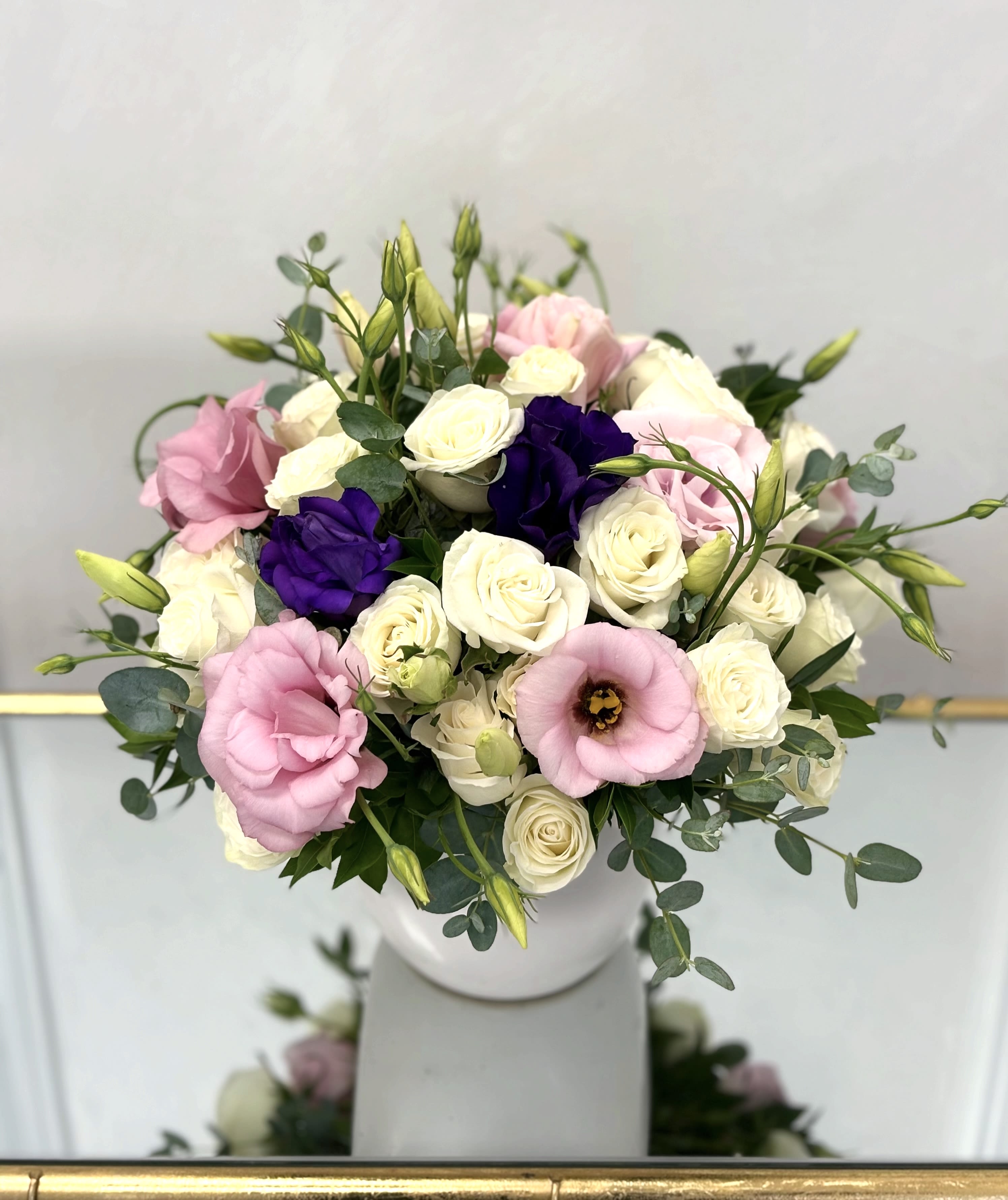 Purple Touch By VLM Flowers - Purple Touch is a graceful blend of ivory roses and blush lisianthus, softly accented by elegant purple blooms for a hint of depth and drama. This delicate composition evokes feelings of calm, affection, and understated elegance. Designed in a modern white vase, it’s perfect for thoughtful gestures, sympathy, or simply bringing a touch of serenity to any space.