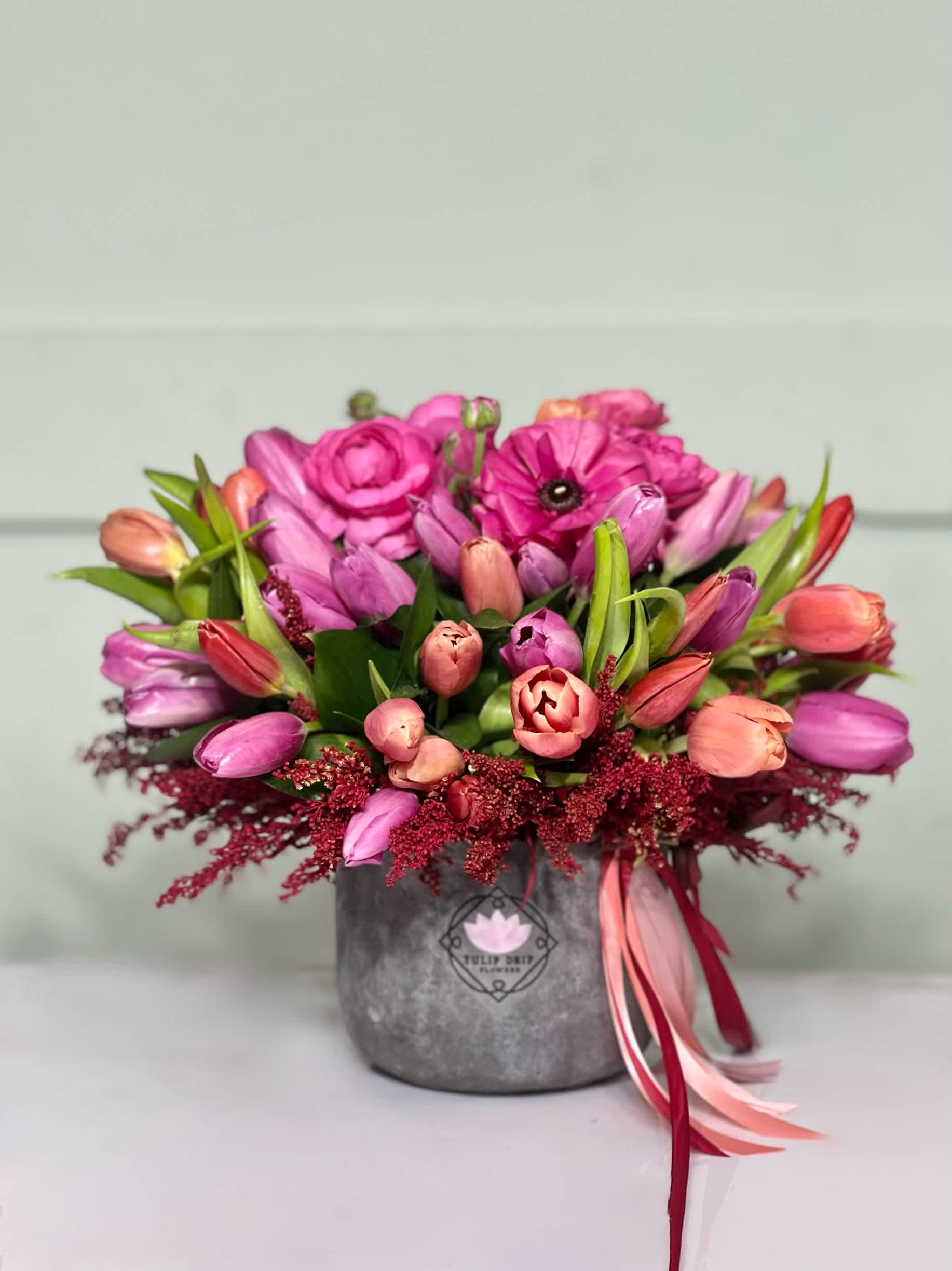 Pink and peach tulips arranged in a gray vase with ribbon