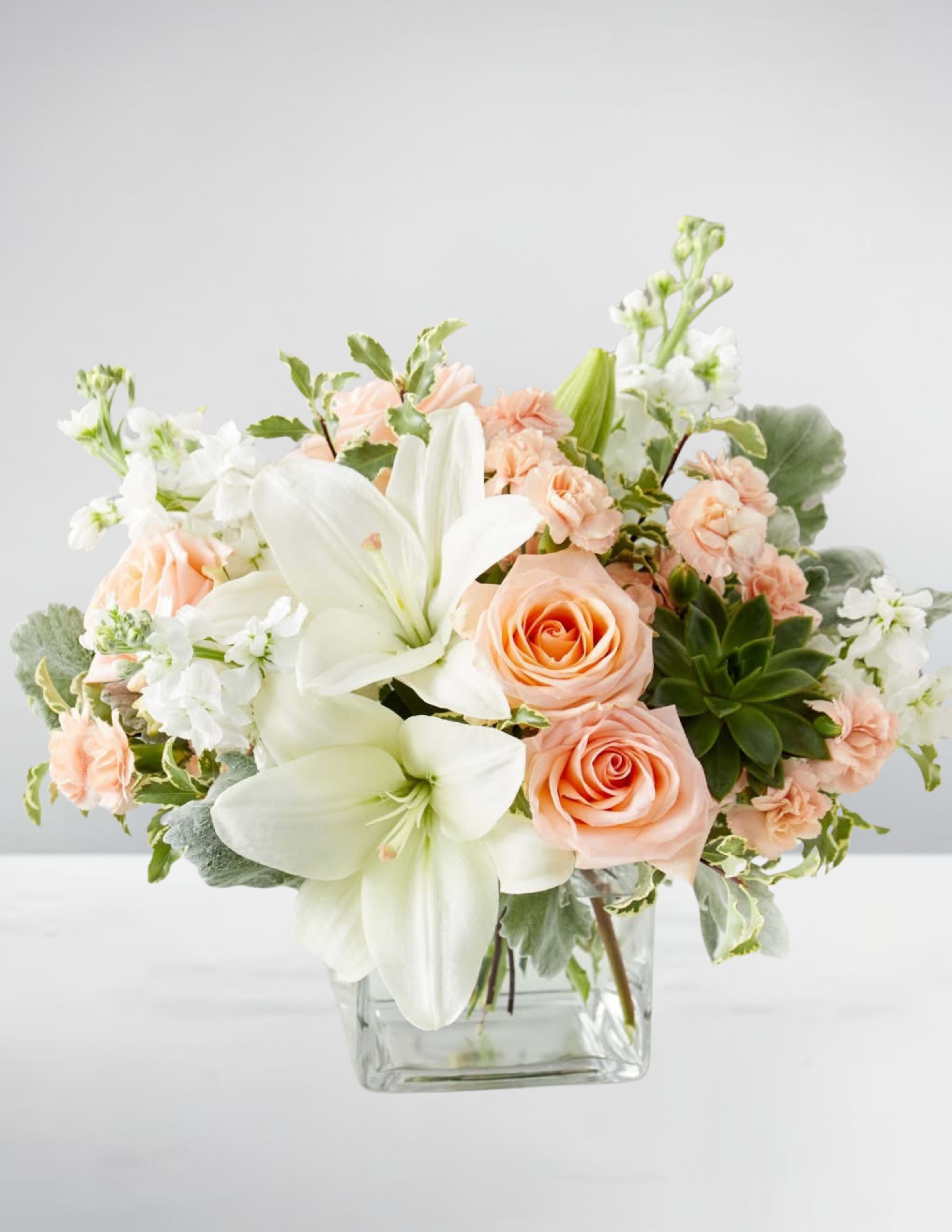 Blushing blooms - "Blushing Blooms" is a delicate and charming floral arrangement that exudes elegance and sophistication. The bouquet features a mix of soft pink roses, white lilies, and stock, carefully arranged in a clear glass vase to showcase their beauty. The pastel colors and lush greenery create a romantic and feminine atmosphere, making it perfect for special occasions or as a gift. The compact size of the bouquet adds to its charm, making it ideal for small spaces or as a centerpiece. Overall, "Blushing Blooms" is a beautiful and timeless floral arrangement that is sure to delight.
