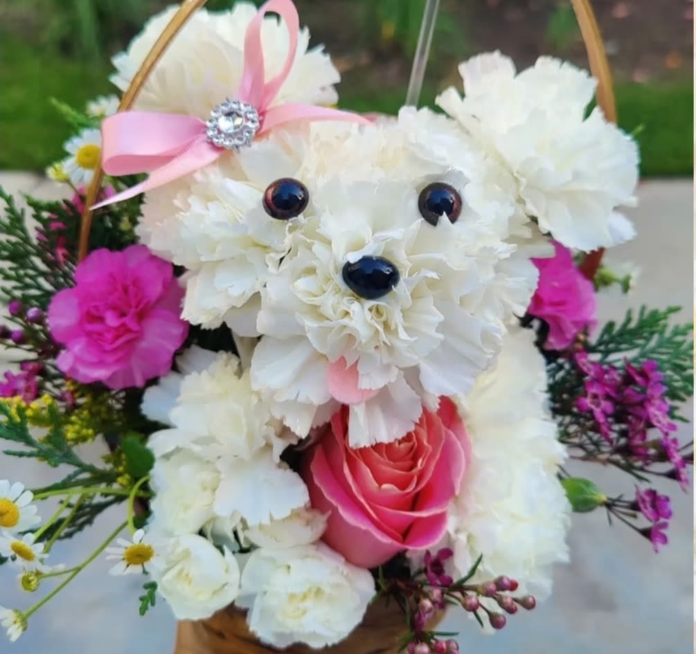 " Dory " Cute Floral Puppy. - It’s so  cute. A charming  puppy arrangement crafted  with fancy white carnations,  seasonal  premium flowers in pink and white  tones:  roses, mini carnations, pompon flowers, fragrant wax flowers and seasonal greenery. It  comes in  a rustic basket. Medium size  It’s perfect for birthday, just because, thank you, congratulations,    