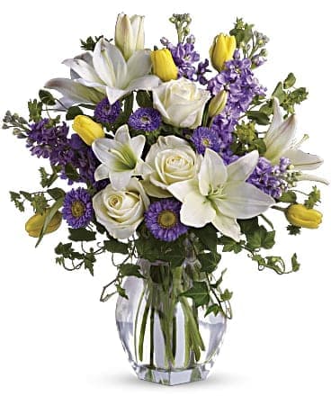 Spring Waltz Bouquet - Dance into spring! Send this feminine bouquet of favorite spring flowers to brighten someone's home with the playful beauty of nature. Such a pretty way to say, "I'm thinking of you!" This white, lavender and yellow bouquet includes white asiatic lilies, cream roses, yellow tulips, lavender stock, lavender matsumoto asters and greens including bupleurum, ivy and seeded eucalyptus. Delivered in a gorgeous vase.     