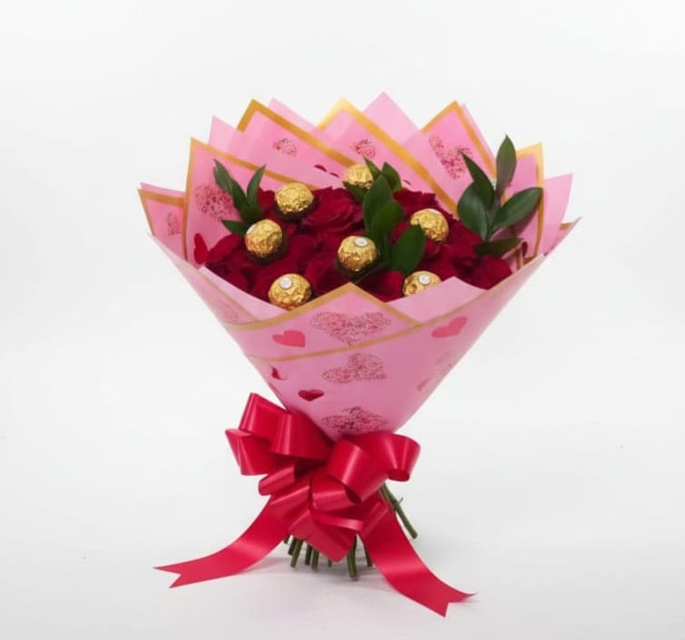 Blushing Love Bouquet - This elegant arrangement combines 20 red roses with delicious Ferrero Rocher chocolates, creating the perfect mix of romance and sweetness. The bouquet is wrapped in soft pink decorative floral paper with hear patterns and finished with stylish pink ribbon bow. Paper and ribbon can change color according to the client and materials in hand. Este elegante arreglo de flores combina 20 rosas rojas con deliciosos chocolates Ferrero Rocher, creando la mezcla perfecta de romance y dulzura. El ramo está envuelto en papel floral decorativo de color rosa suave con patrones de corazones y terminado con un elegante lazo de cinta rosa. El papel y la cinta pueden cambiar de color de acuerdo al cliente y los materiales disponibles.